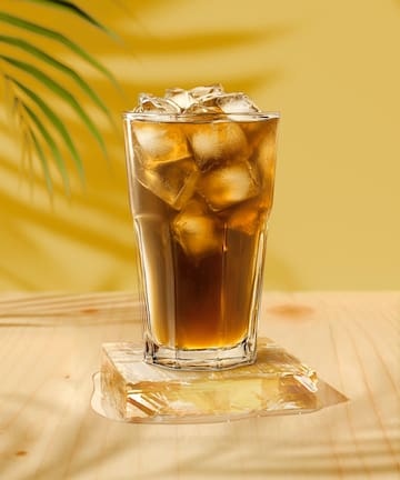 a glass of ice tea with brown liquid on a wooden surface