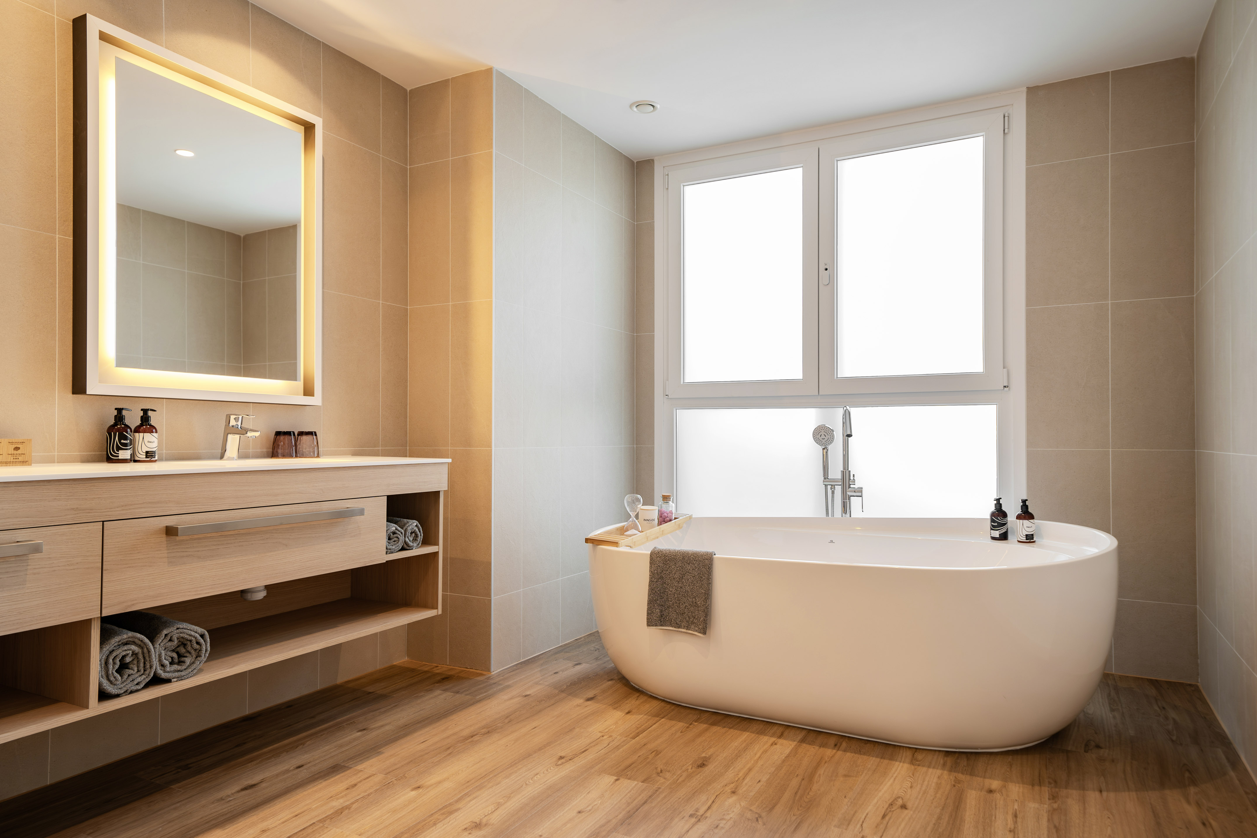 Modern bathroom with freestanding bathtub, wood vanity, and backlit mirror.
