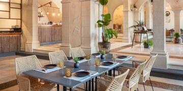 a table with plates and wicker chairs in a room with columns and a bar