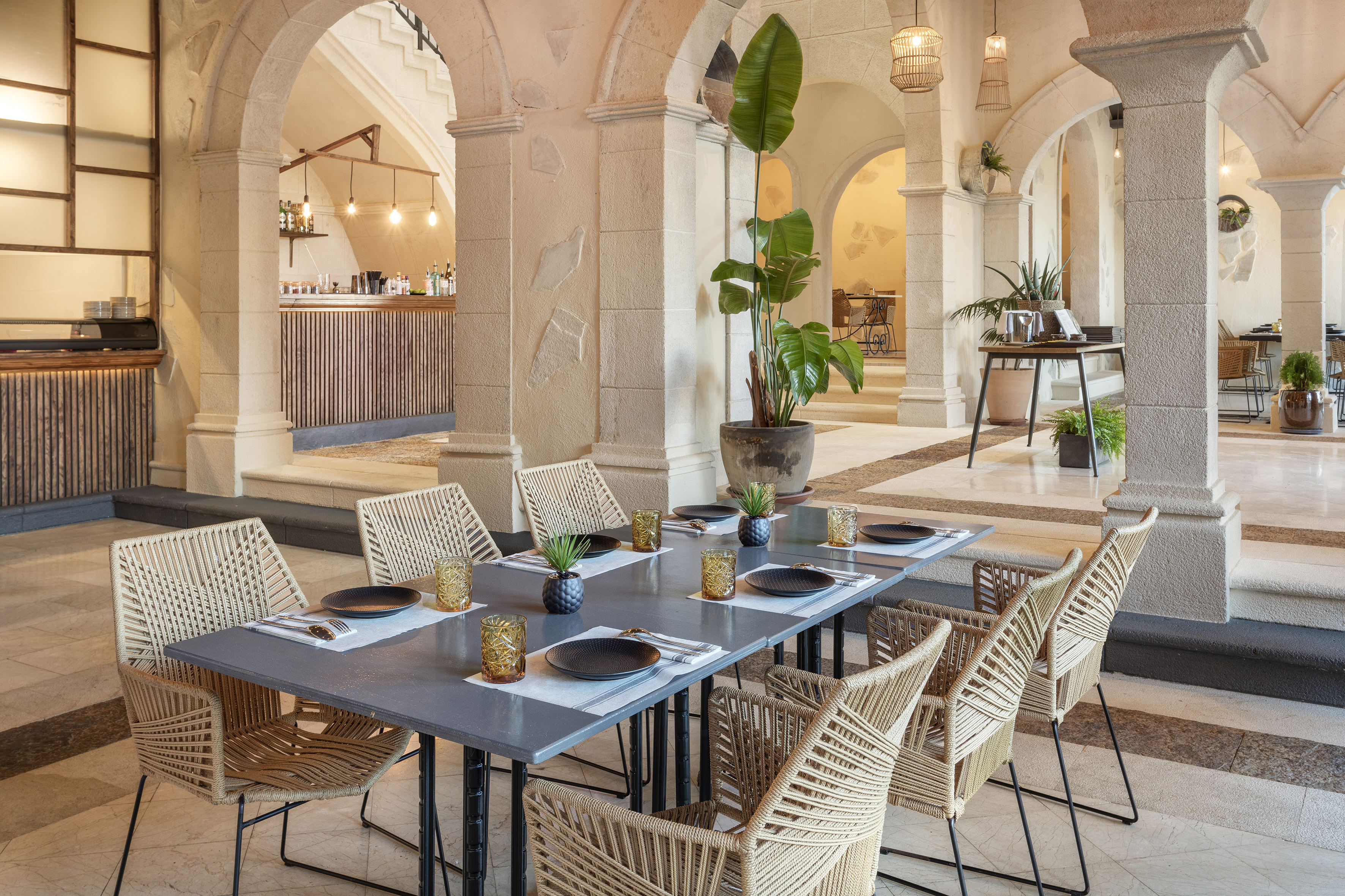 Elegant restaurant dining area with stone arches, bar, and modern woven chairs.