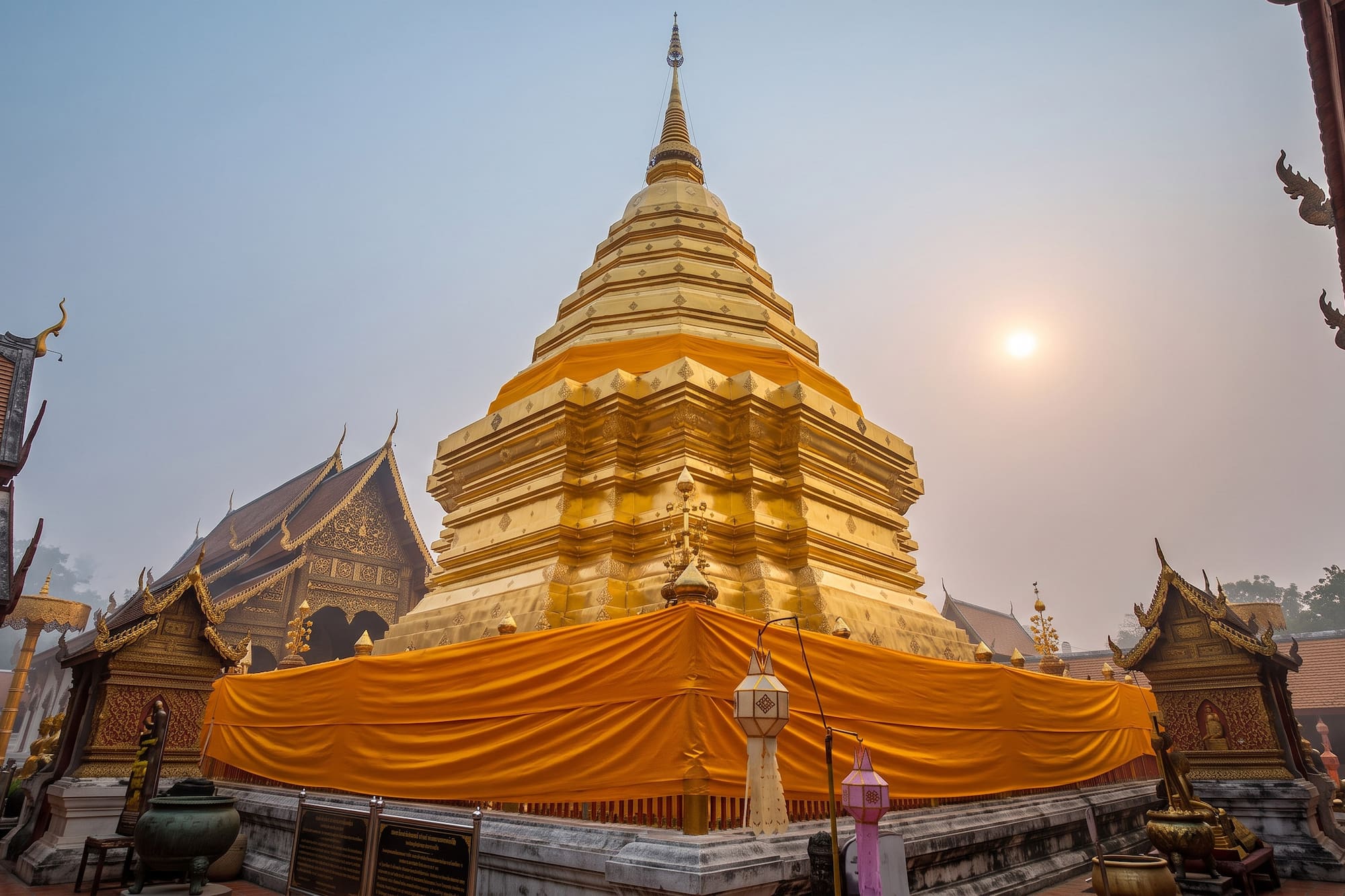 Golden Buddhist stupa wrapped in orange fabric under a hazy sun.