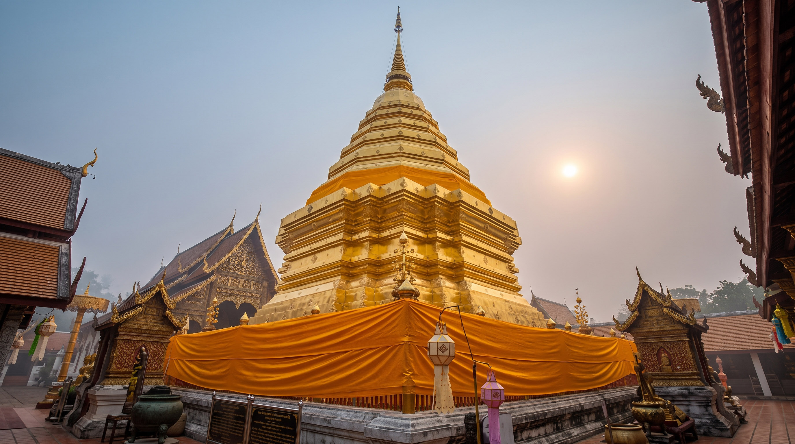 Golden Buddhist stupa wrapped in orange fabric under a hazy sun.
