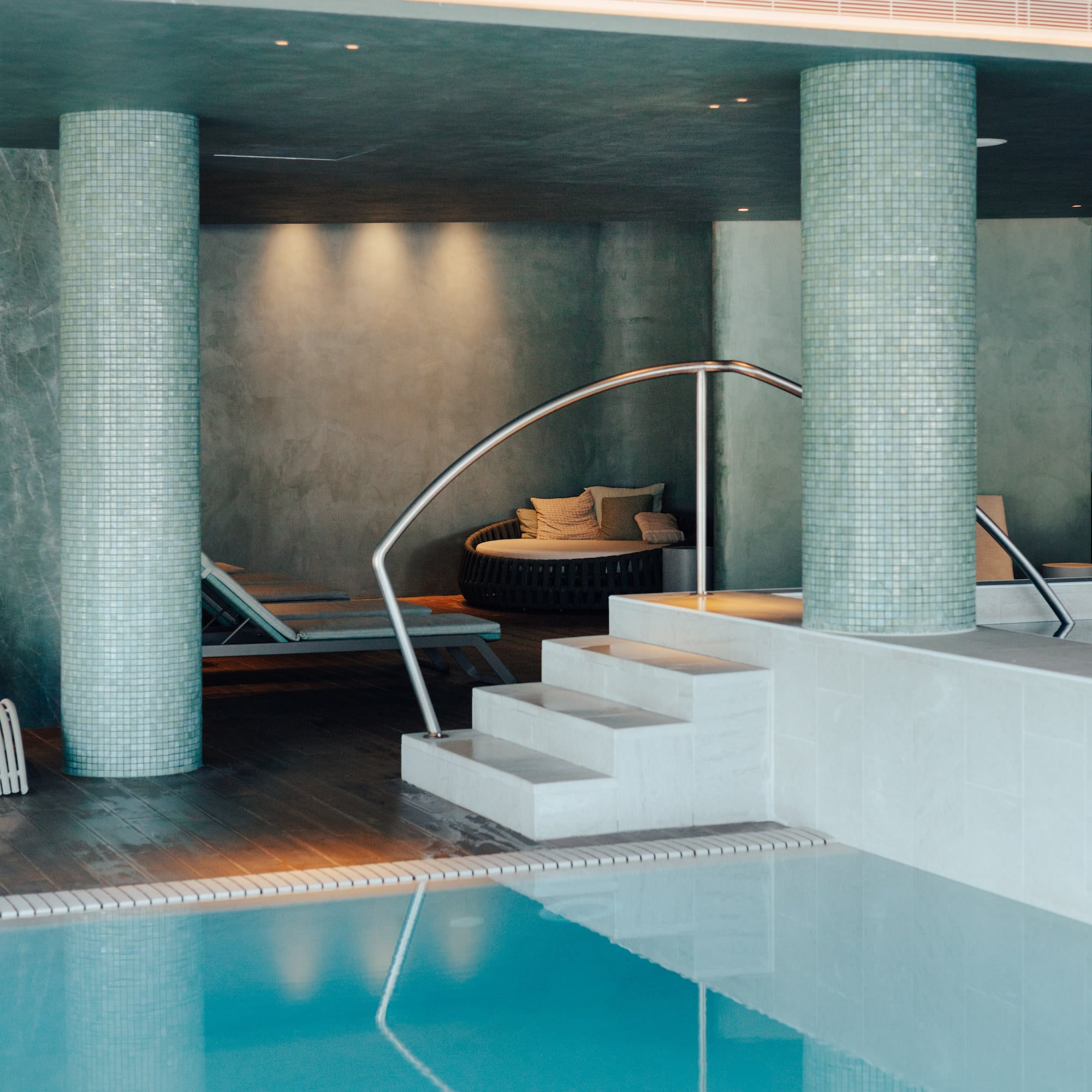 Serene indoor spa pool featuring mosaic columns, steps, and lounge seating.