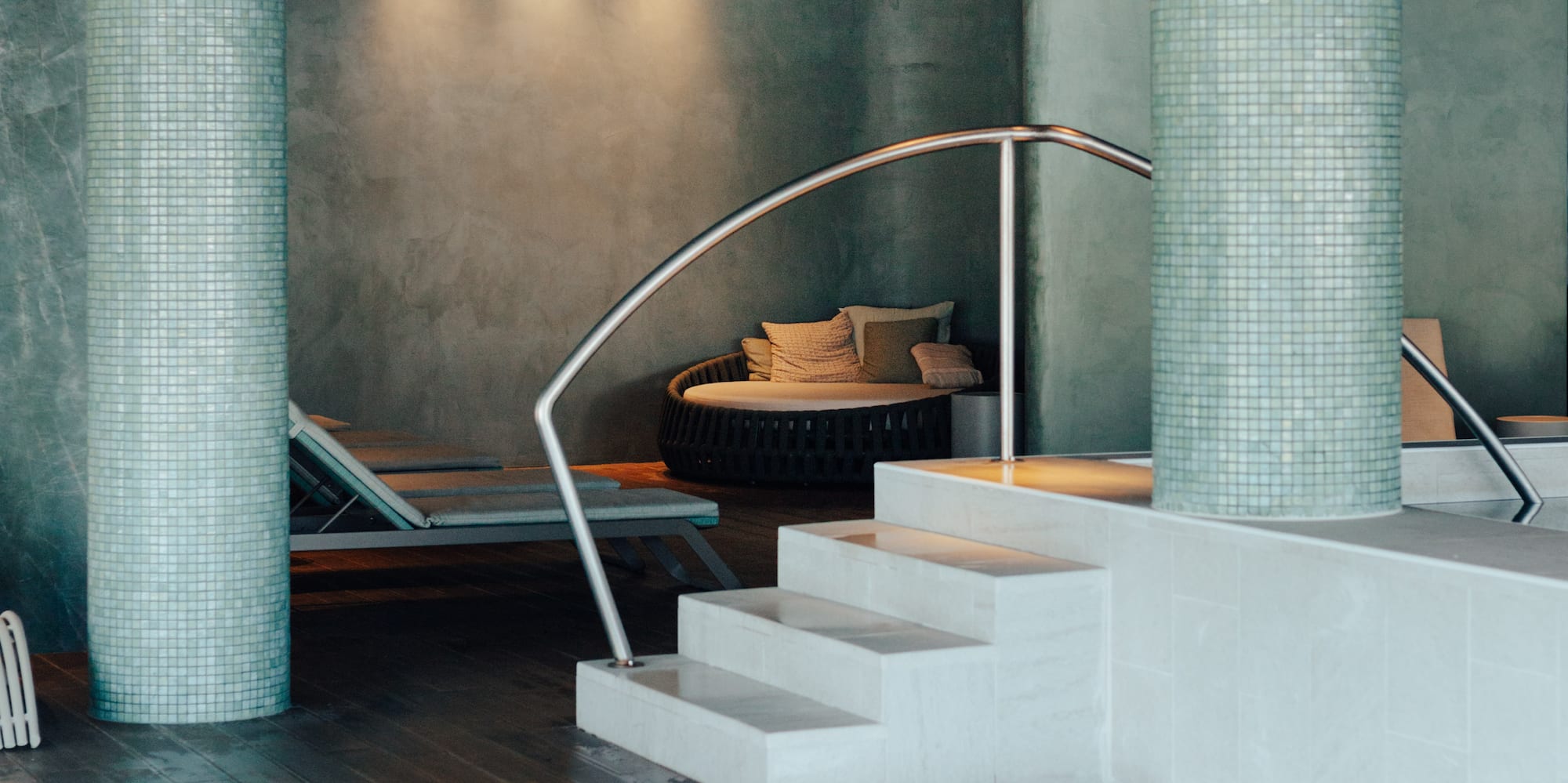 Serene indoor spa pool featuring mosaic columns, steps, and lounge seating.