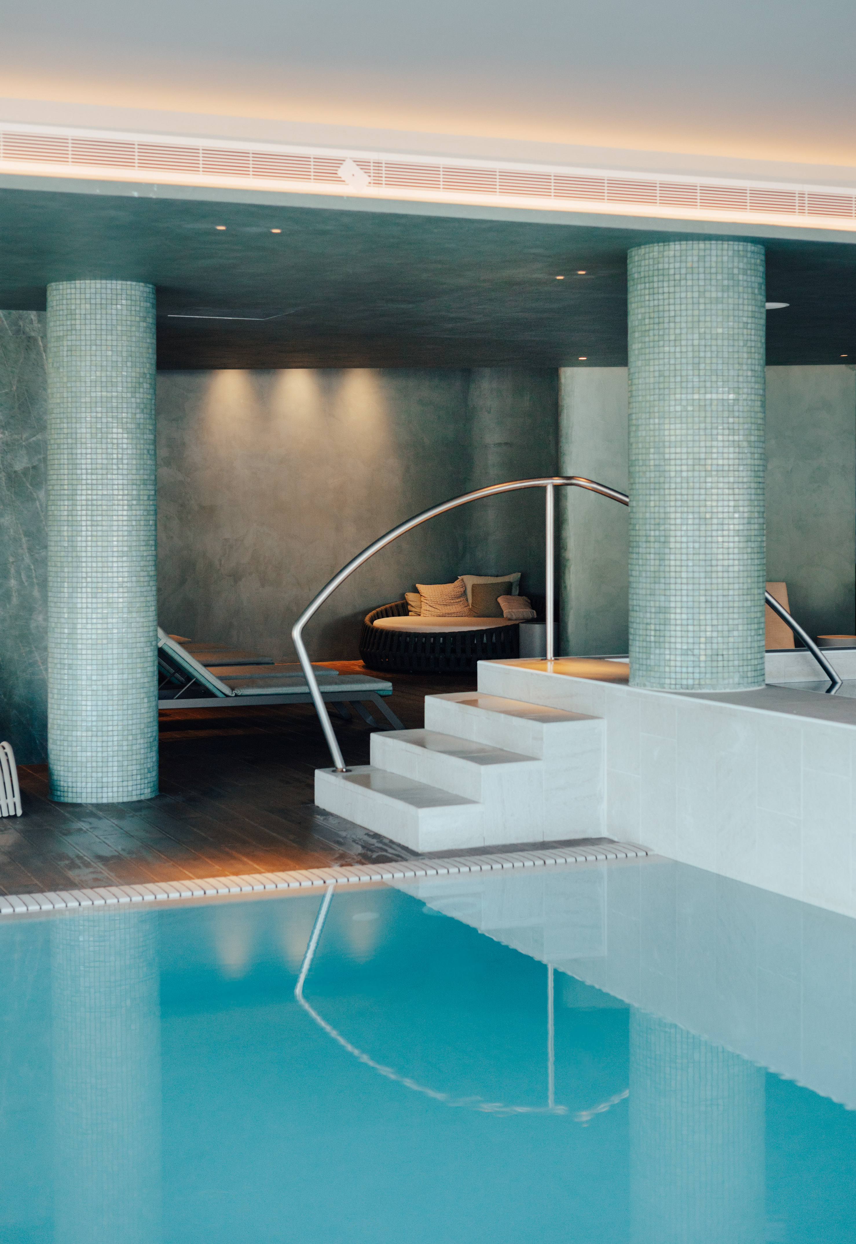 Serene indoor spa pool featuring mosaic columns, steps, and lounge seating.