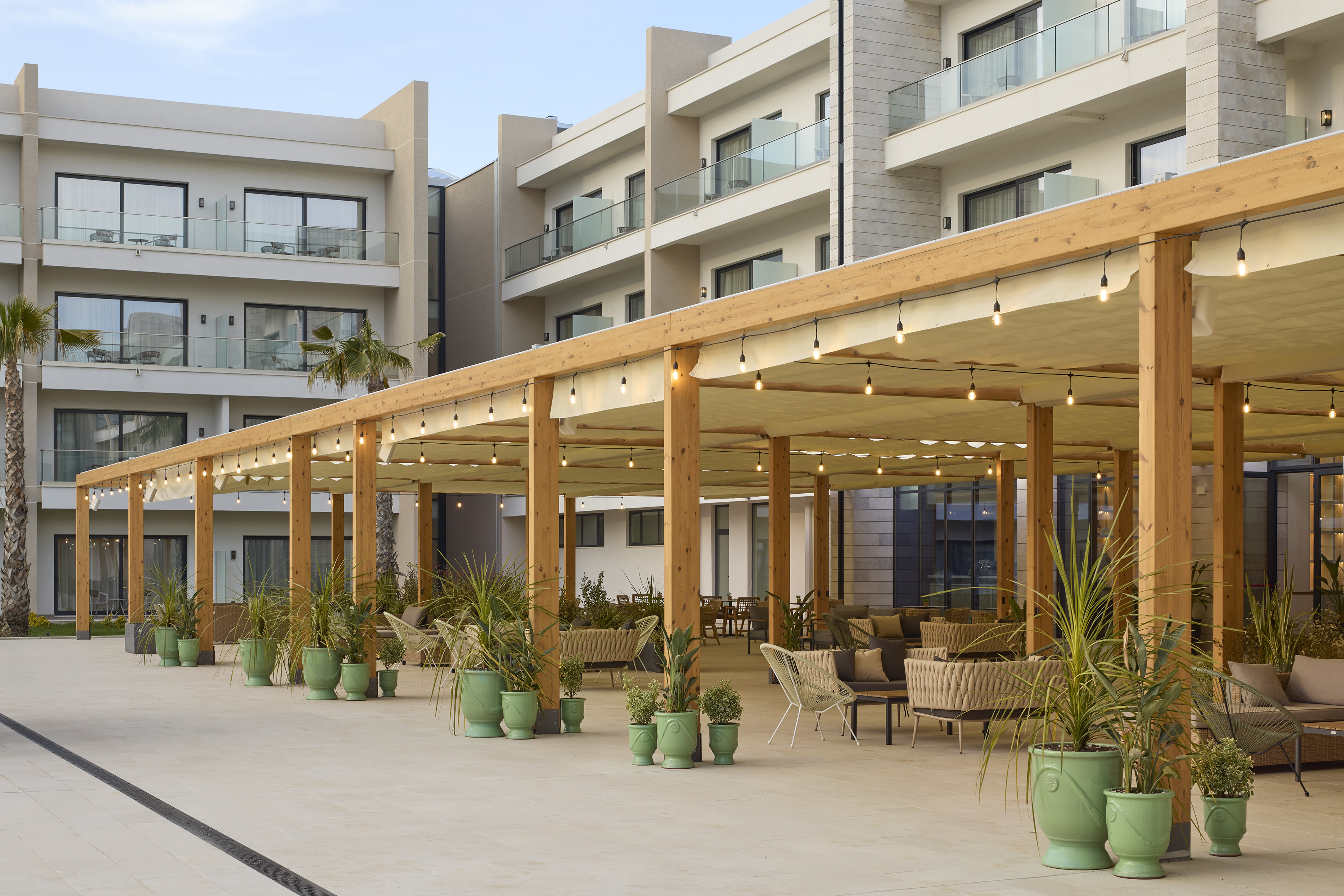 Resort outdoor lounge with wooden pergola, string lights, and lush potted plants.