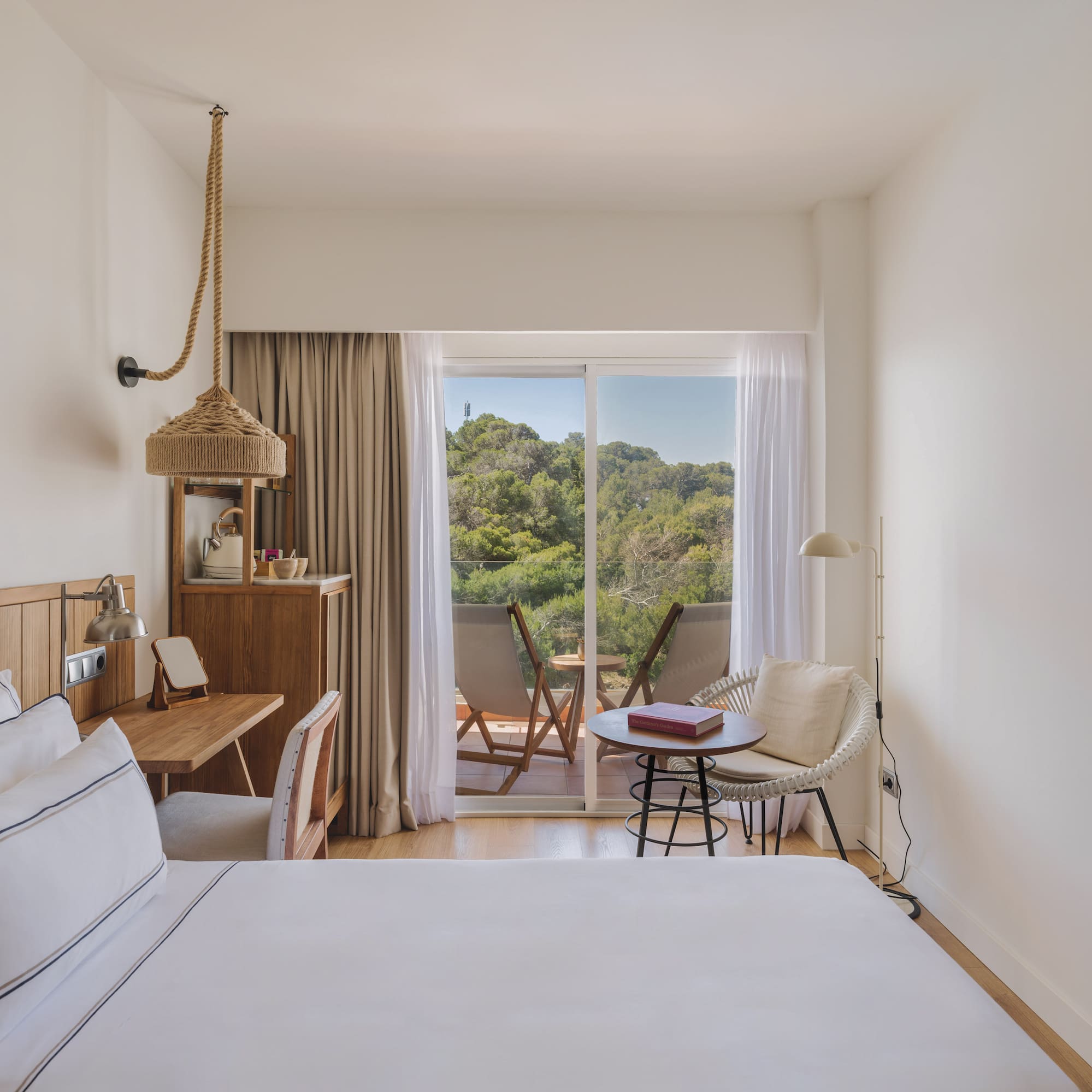 Modern hotel room with white bed, wooden desk, and balcony forest view.