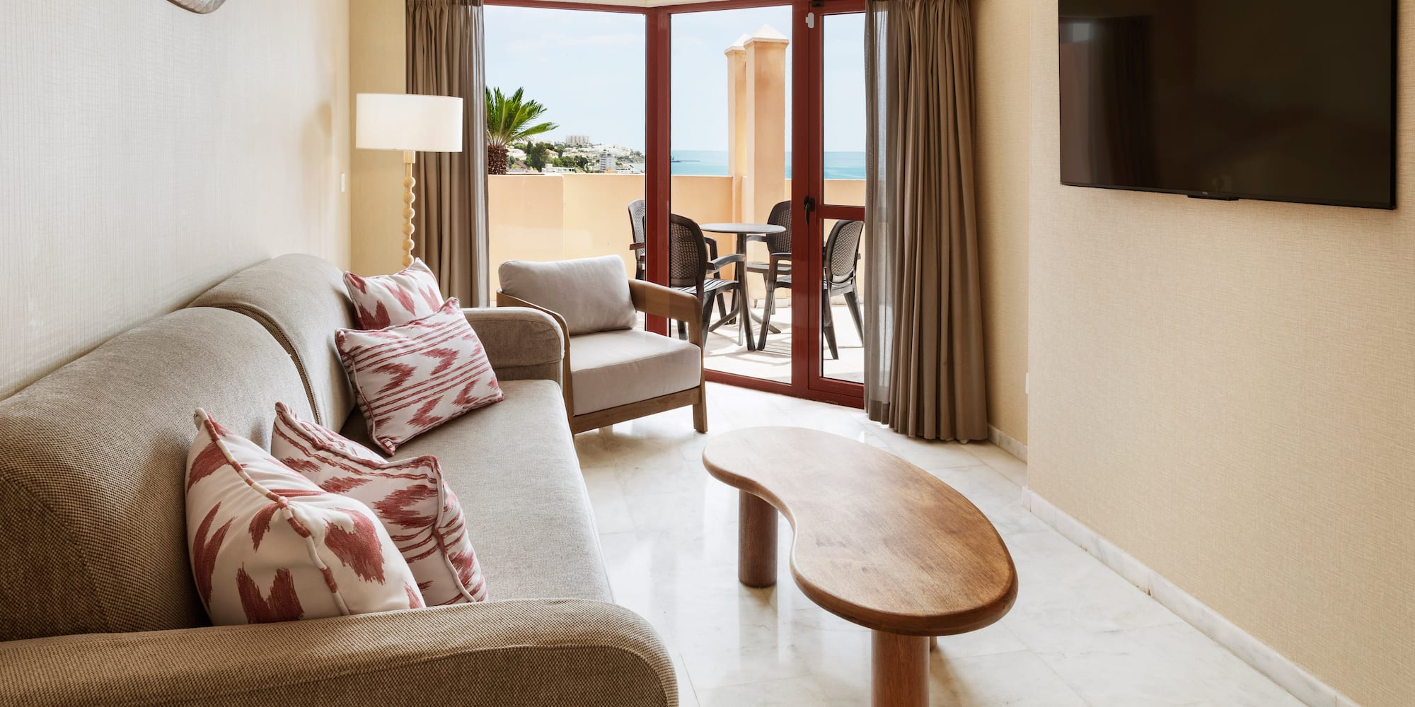 Hotel suite living room with sofa, TV, coffee table, and ocean view balcony.