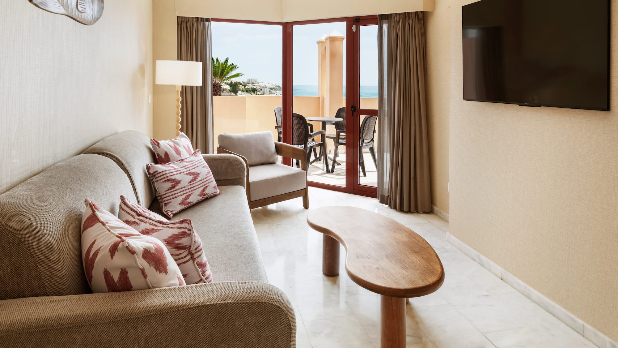 Hotel suite living room with sofa, TV, coffee table, and ocean view balcony.
