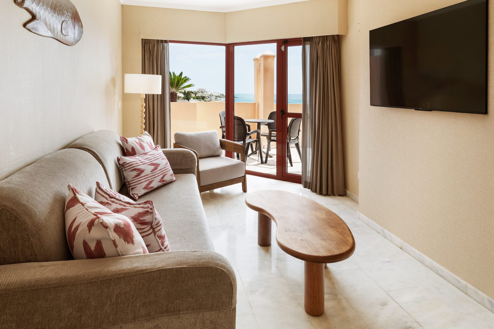 Hotel suite living room with sofa, TV, coffee table, and ocean view balcony.