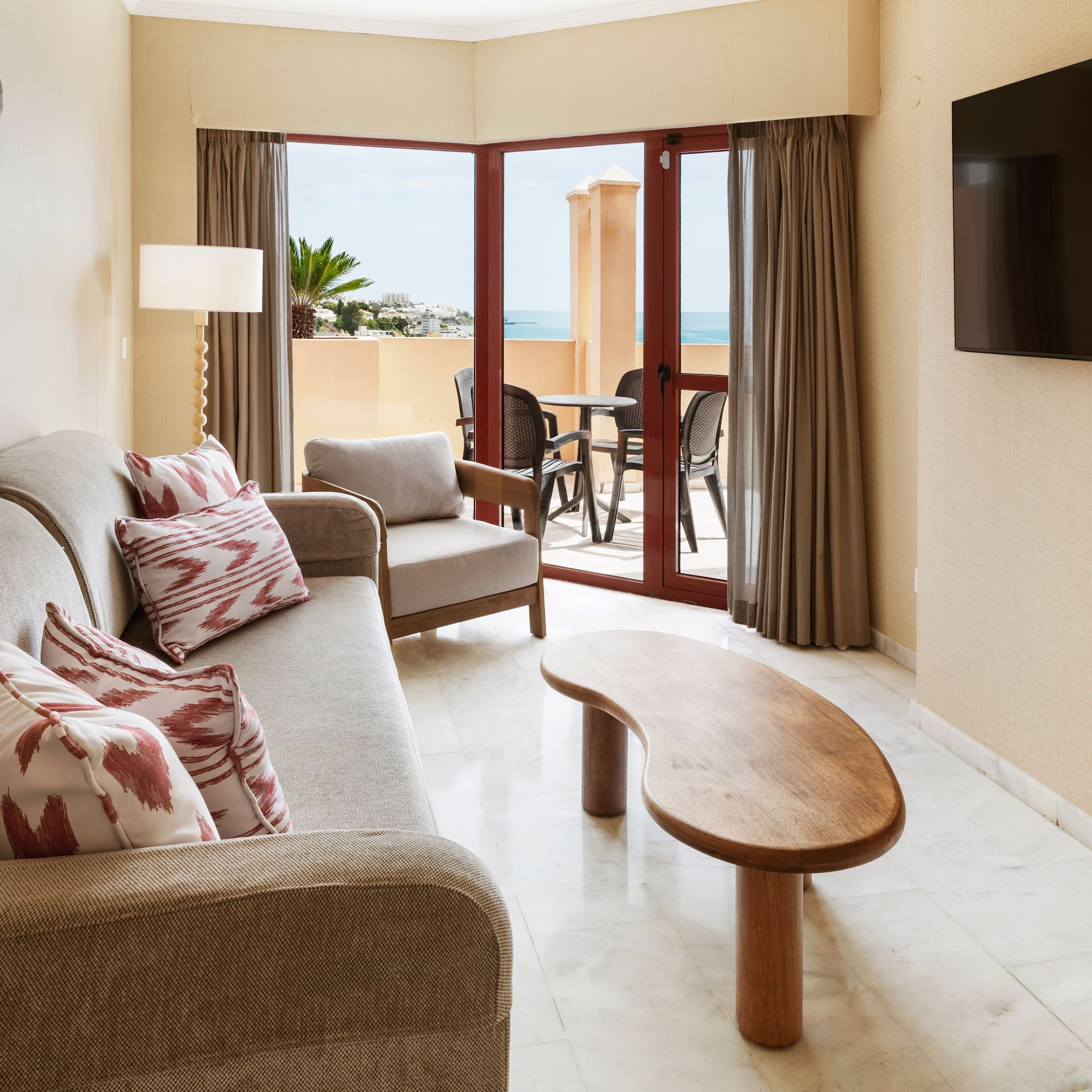 Hotel suite living room with sofa, TV, coffee table, and ocean view balcony.