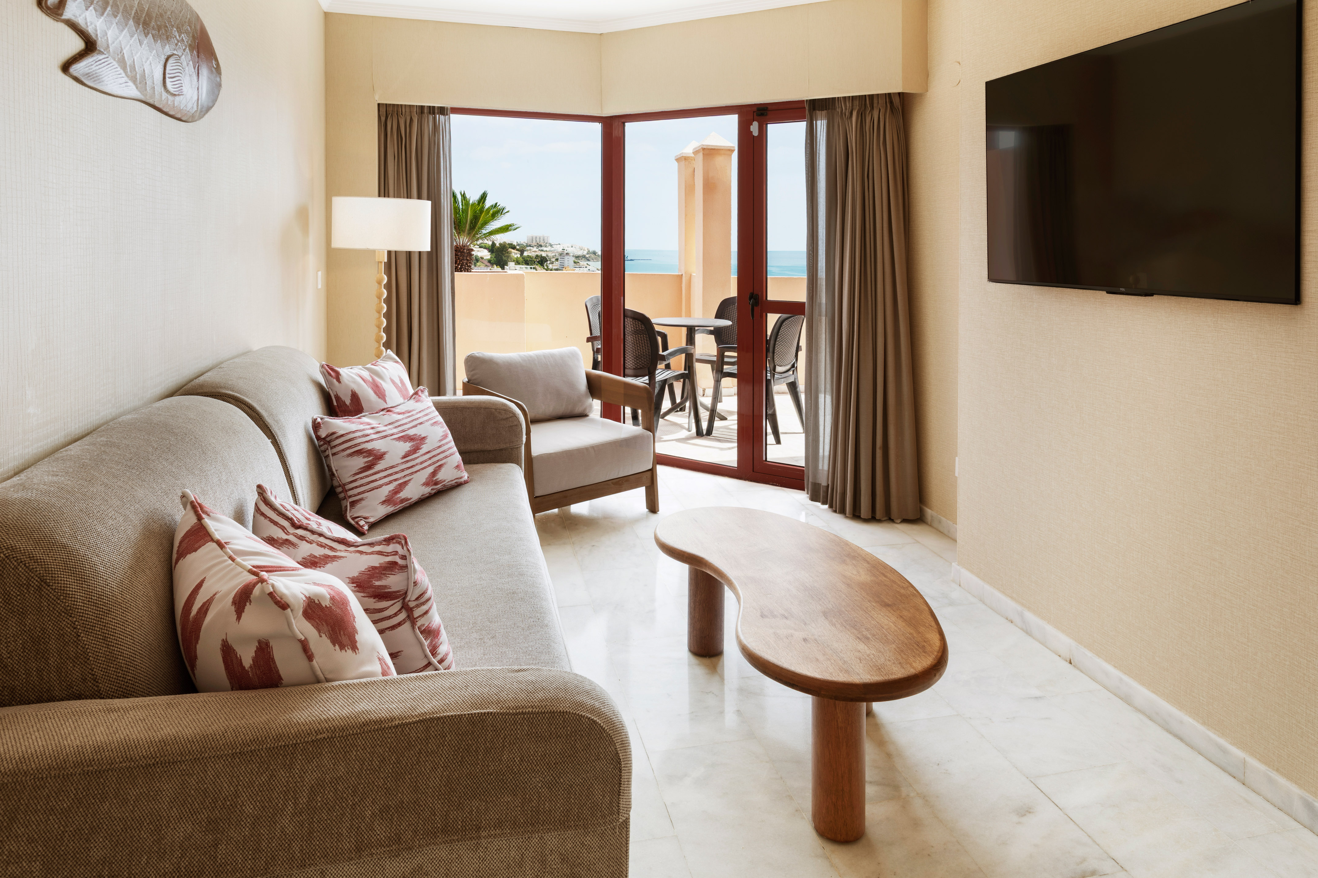 Hotel suite living room with sofa, TV, coffee table, and ocean view balcony.