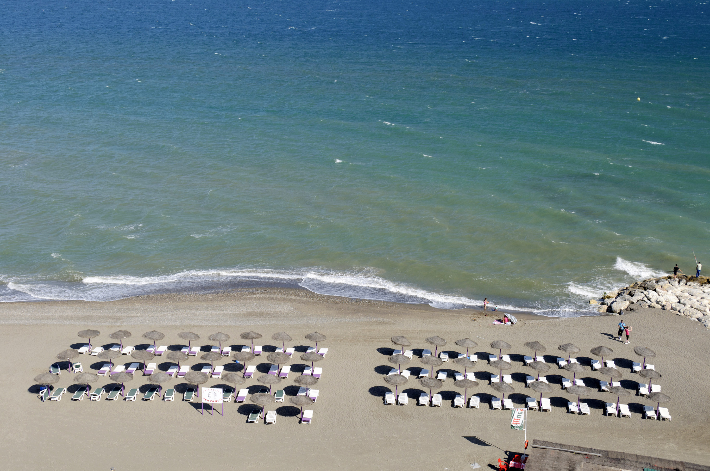 Vista aérea de playa soleada con mar turquesa, sombrillas y tumbonas en la arena.