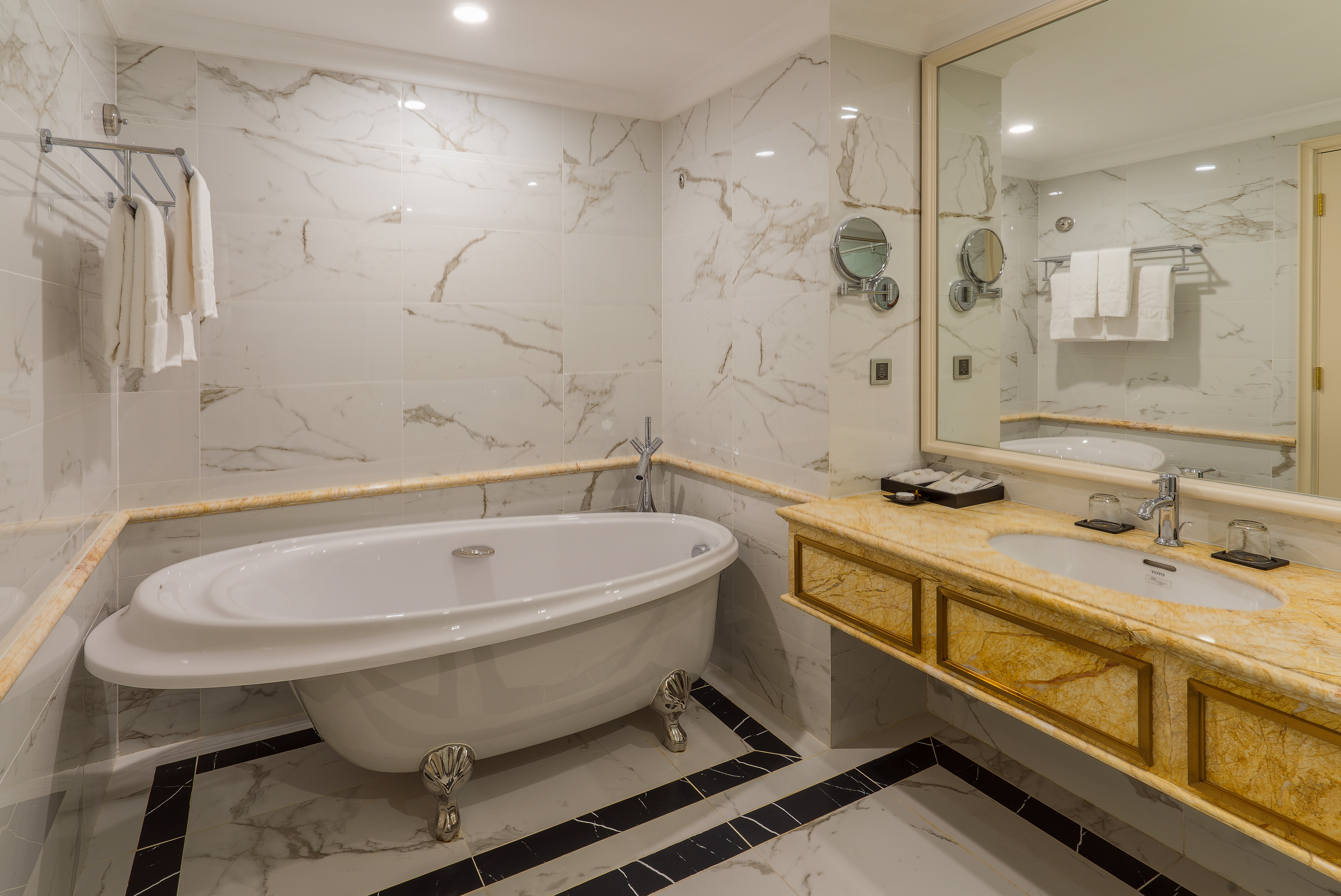 White marble luxury bathroom with clawfoot bathtub and golden vanity.