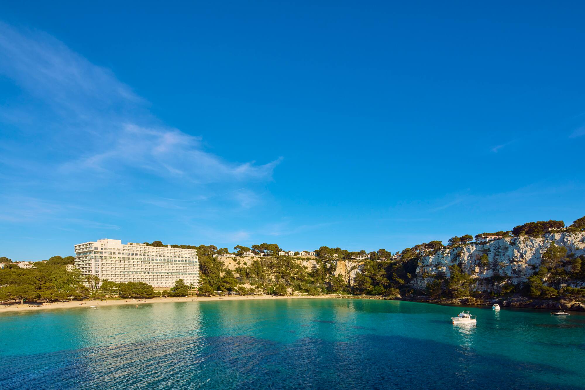 Cala Galdana bay, Menorca: beachfront hotel, sandy beach, turquoise sea, boats.
