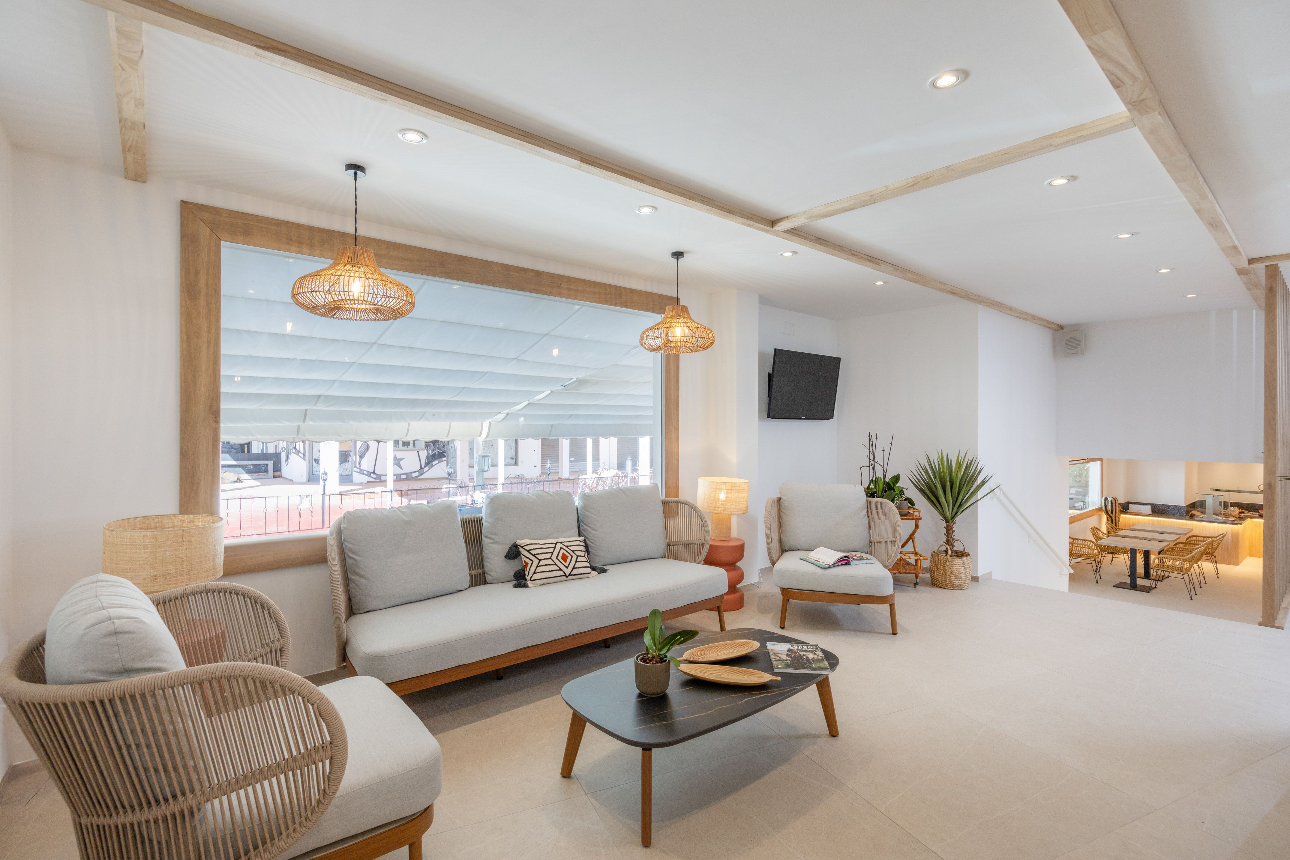 Bright modern lounge with rattan furniture, wooden ceiling, and large window.