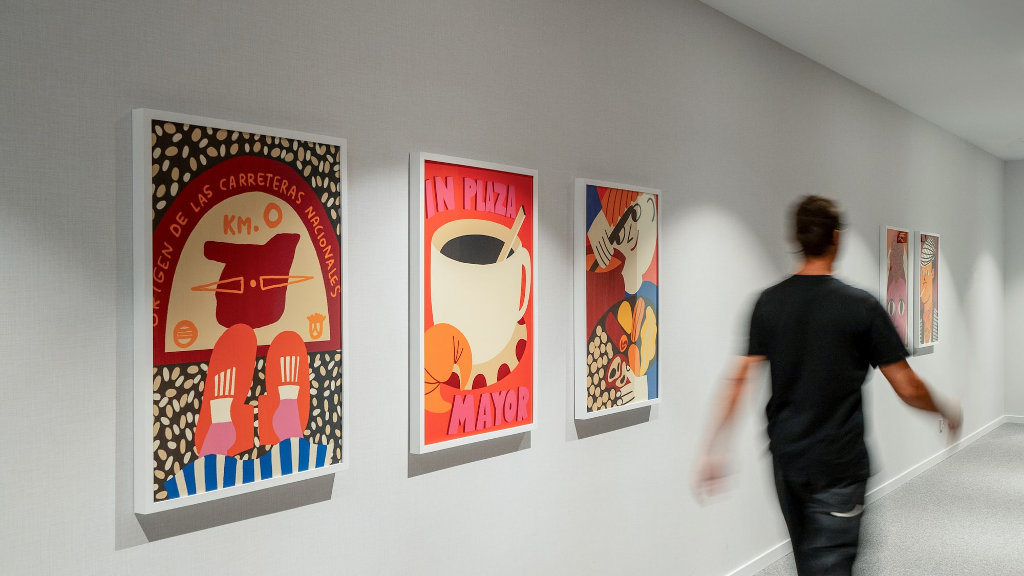 Modern hallway decor with vibrant framed posters and a person in motion.