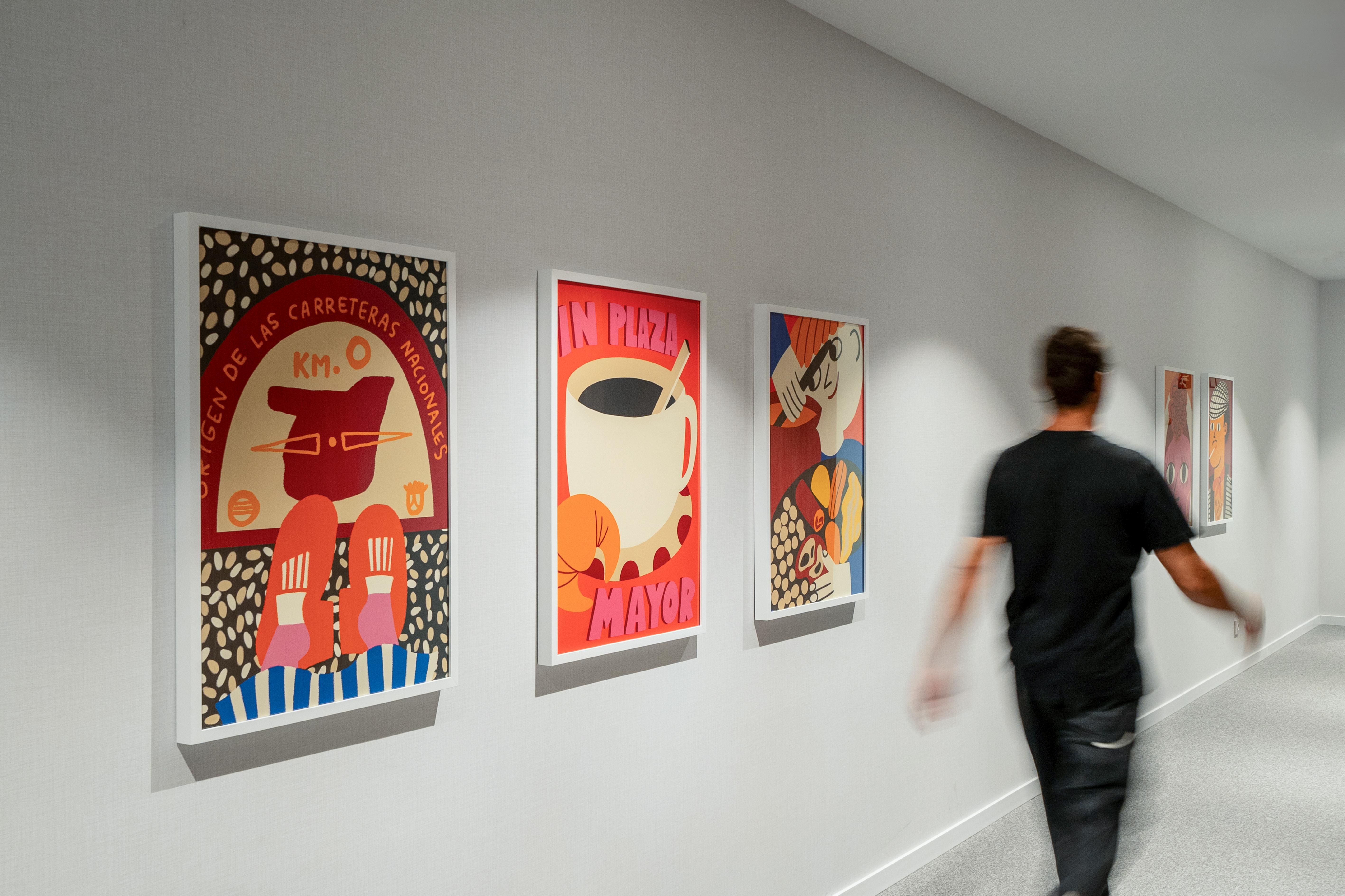 Modern hallway decor with vibrant framed posters and a person in motion.