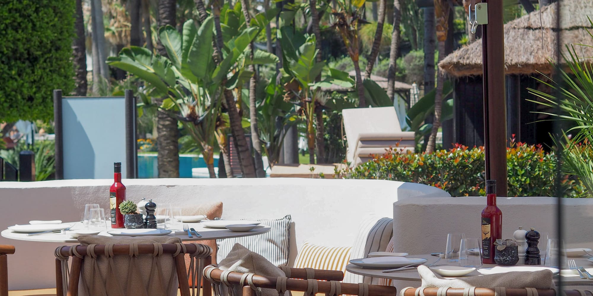 Shaded restaurant patio with wicker chairs, tables, and tropical greenery.