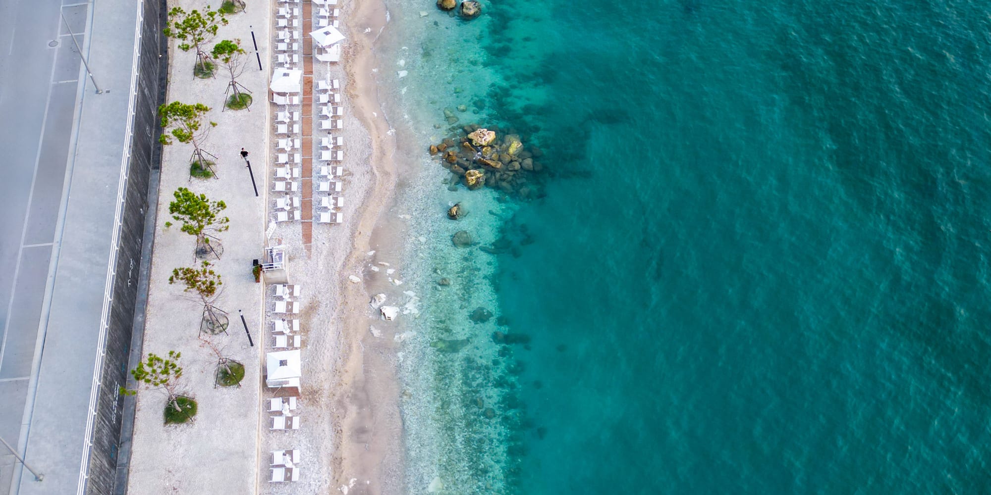 a beach with white chairs and a road next to the water