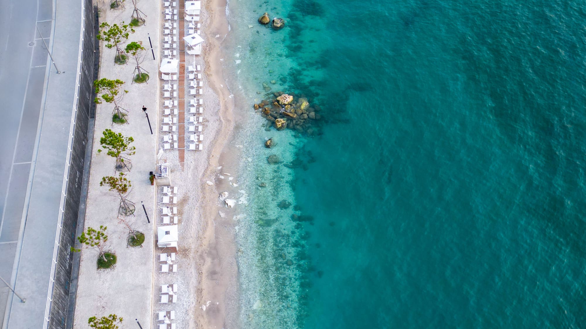 a beach with white chairs and a road next to the water