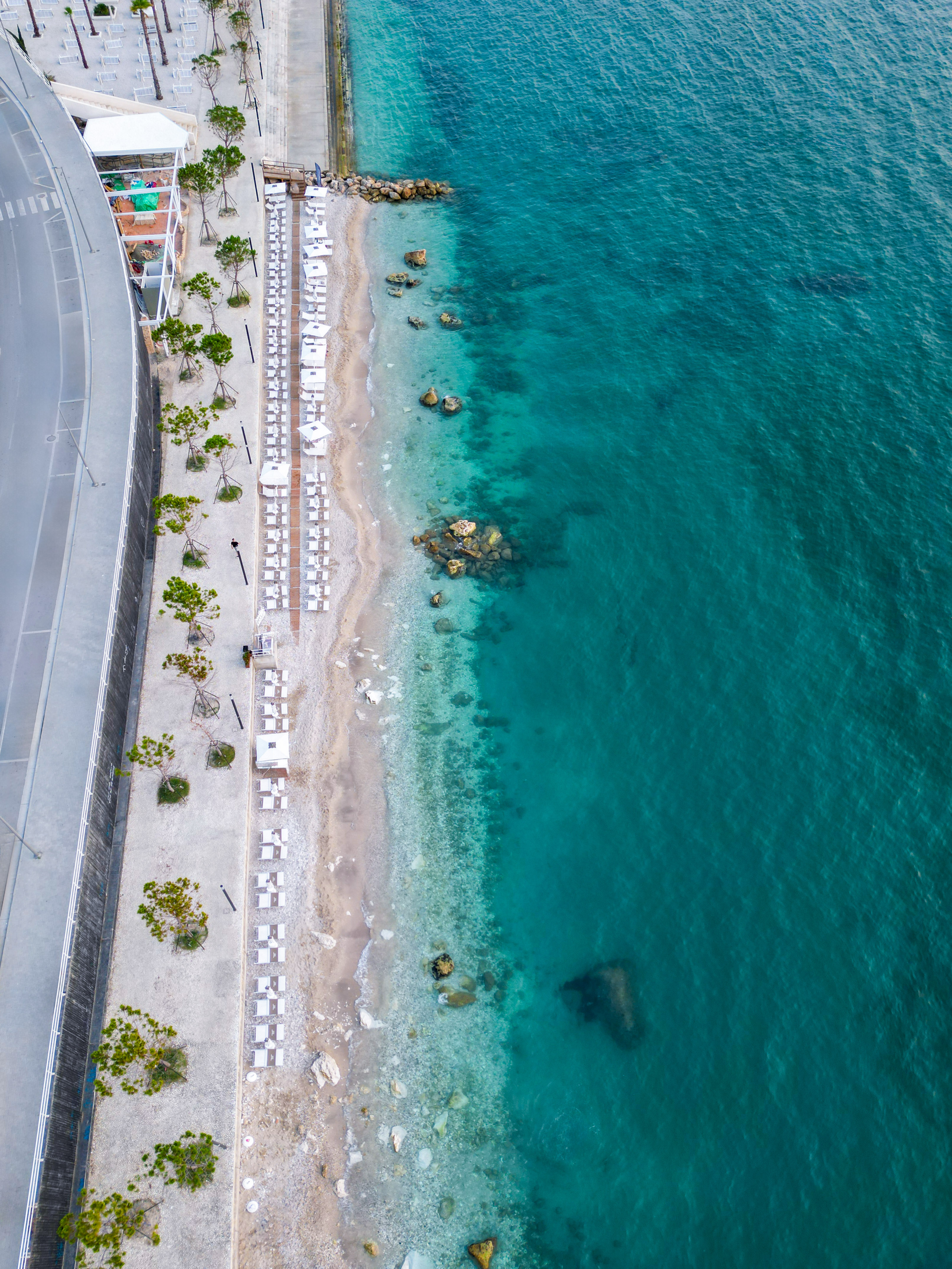 a beach with white chairs and a road next to the water