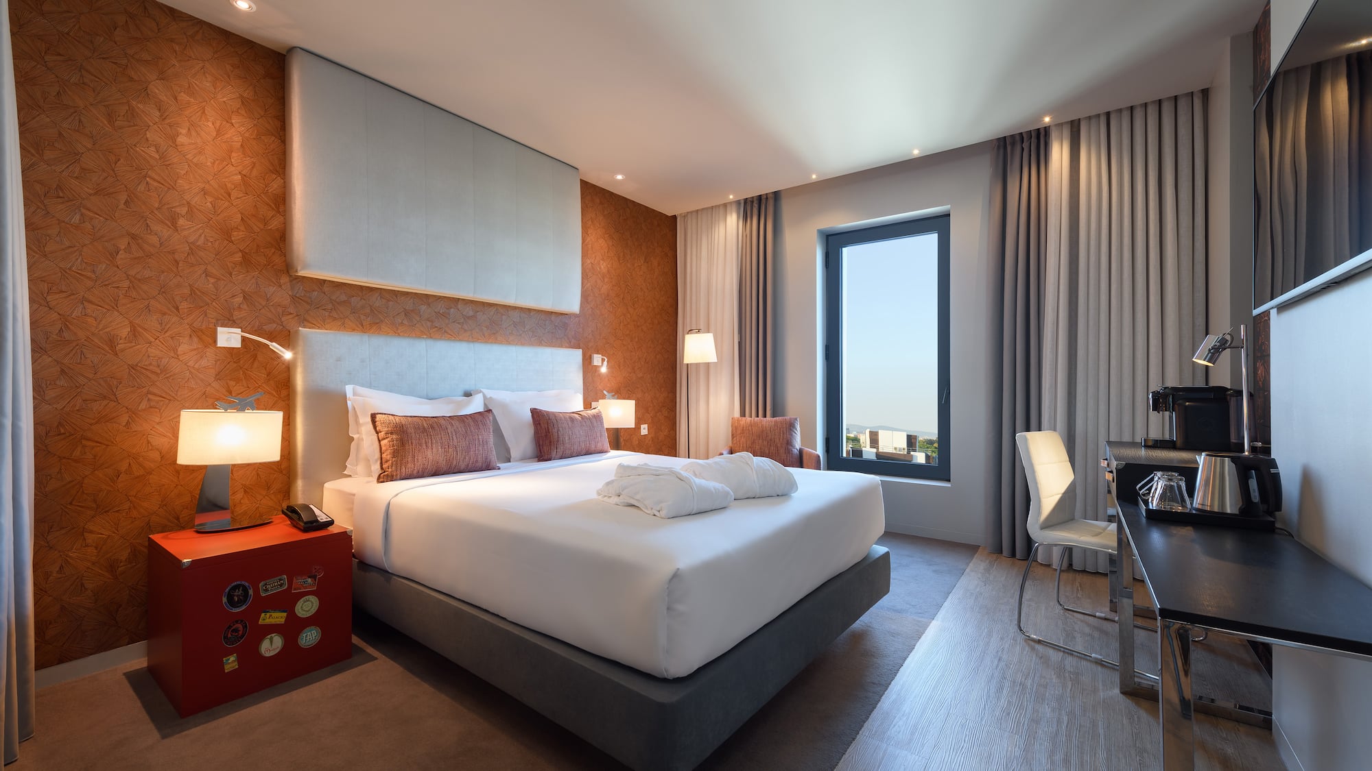 Modern hotel room with large bed, accent wall, desk, and bright window.