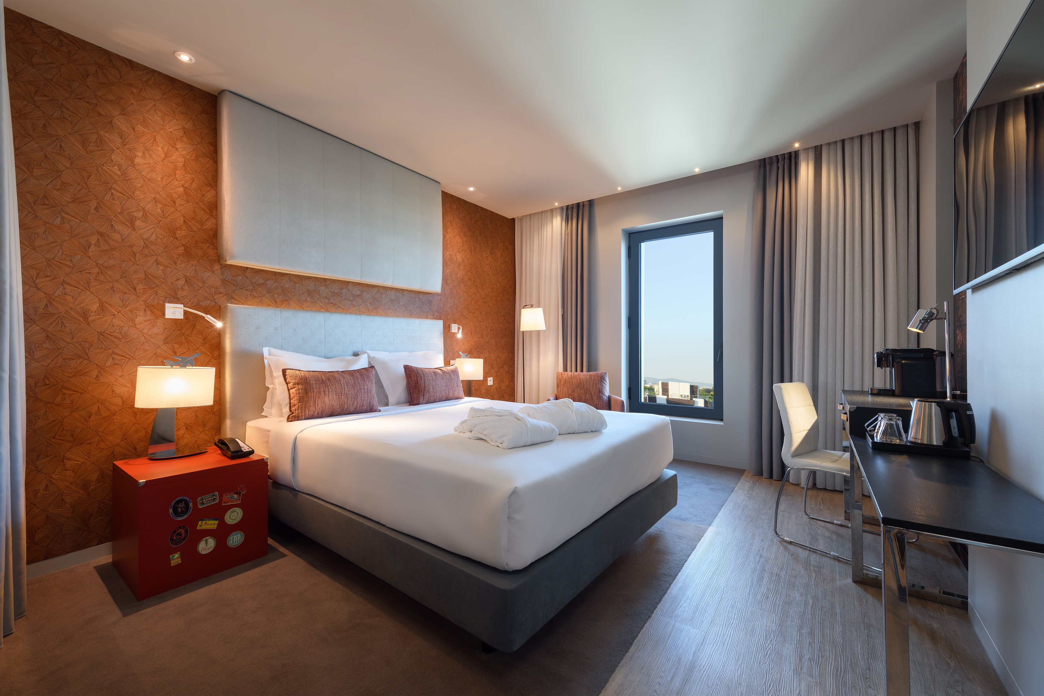 Modern hotel room with large bed, accent wall, desk, and bright window.