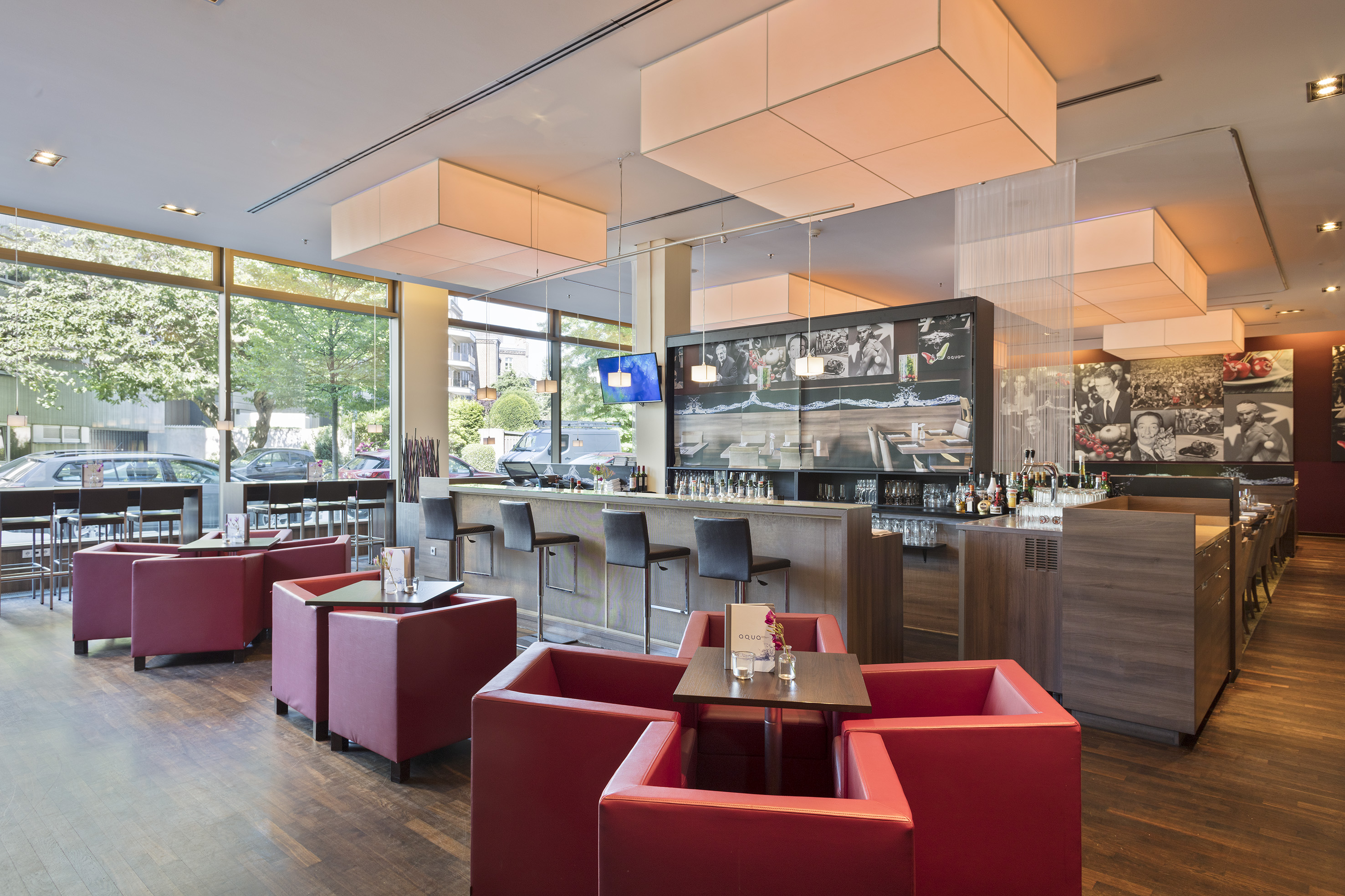 Modern hotel lobby with large windows, street view, wall art, and ceiling lights.
