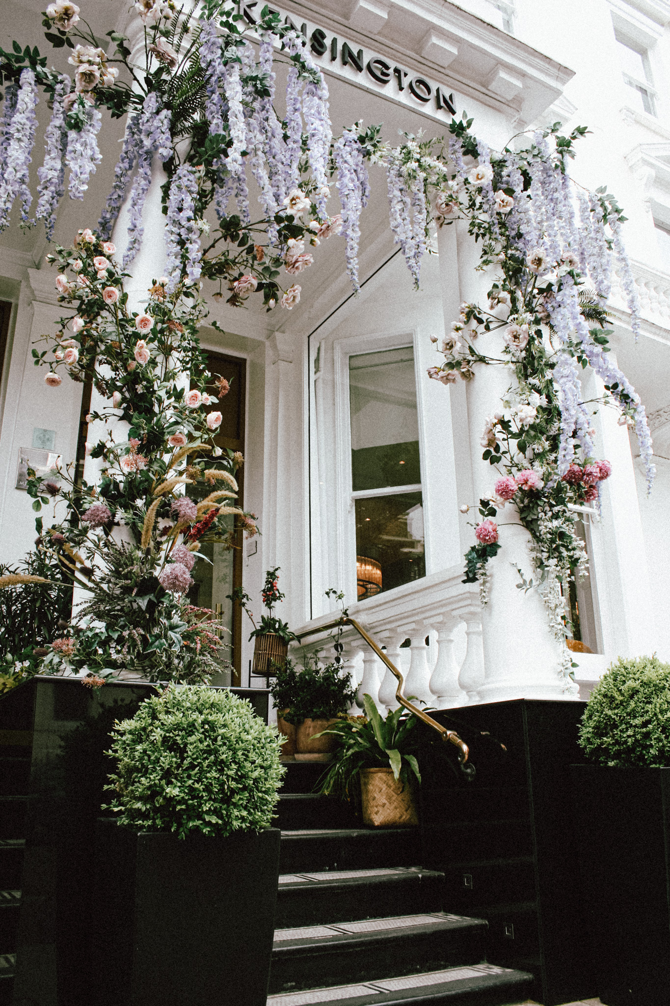a white building with a white column and a white staircase with flowers