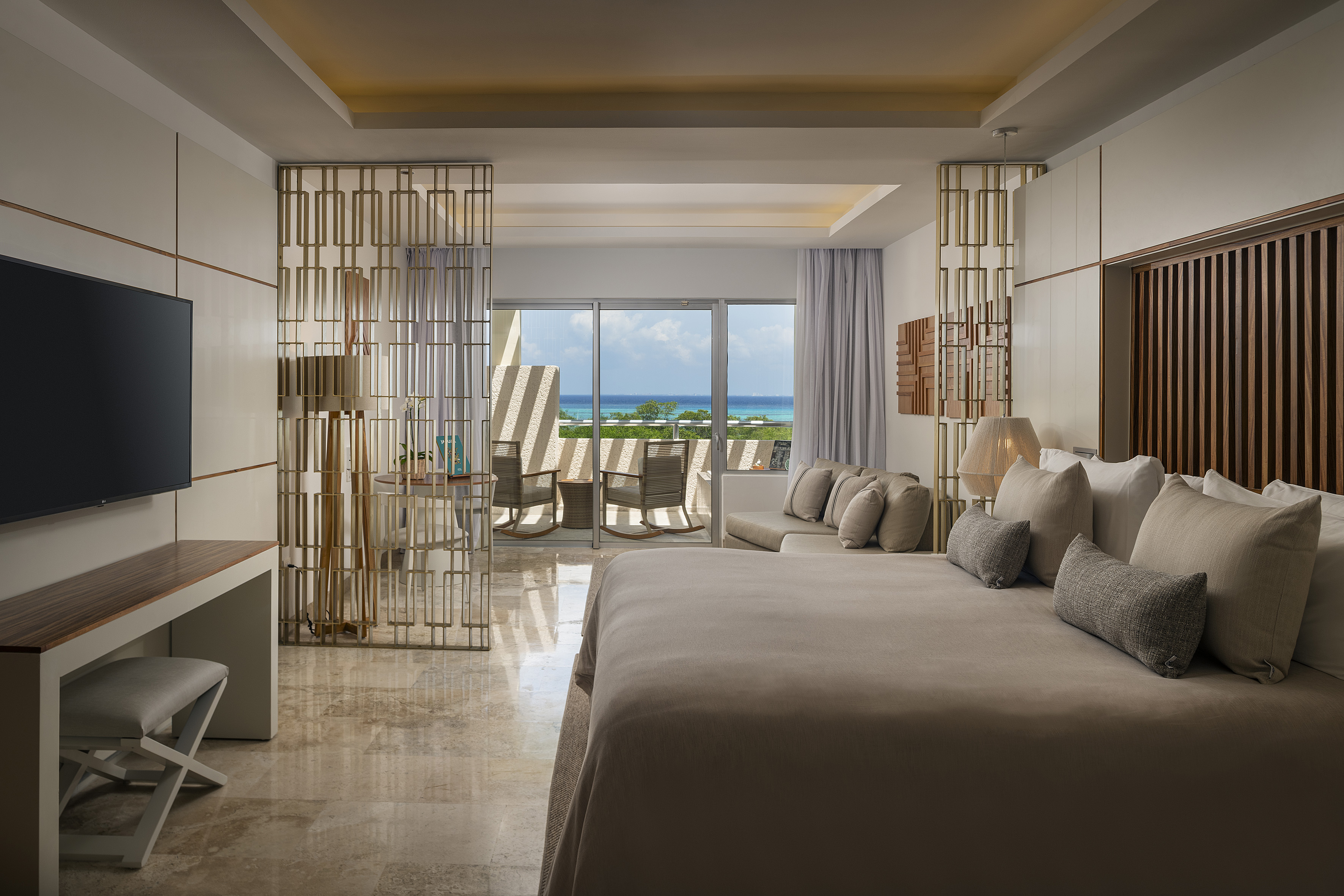 Luxury hotel suite with king bed, ocean view balcony, and modern decor.