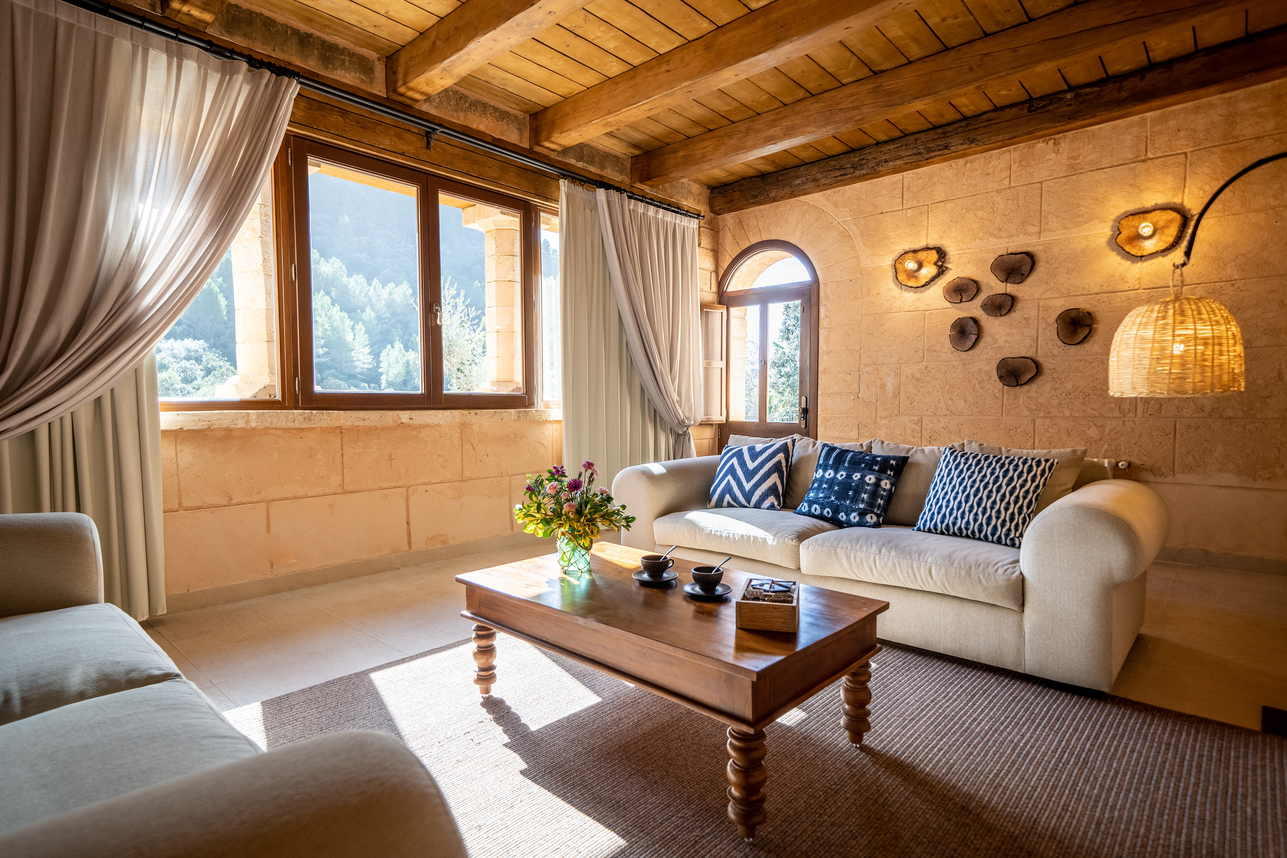 Cozy rustic living room with stone walls, wooden beams, comfortable sofa, and mountain view.
