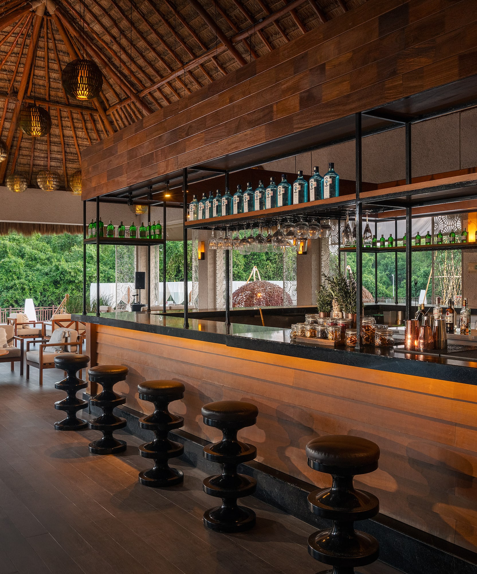 Thatch-roofed tropical bar, ocean view, dark wooden counter, and liquor bottles.
