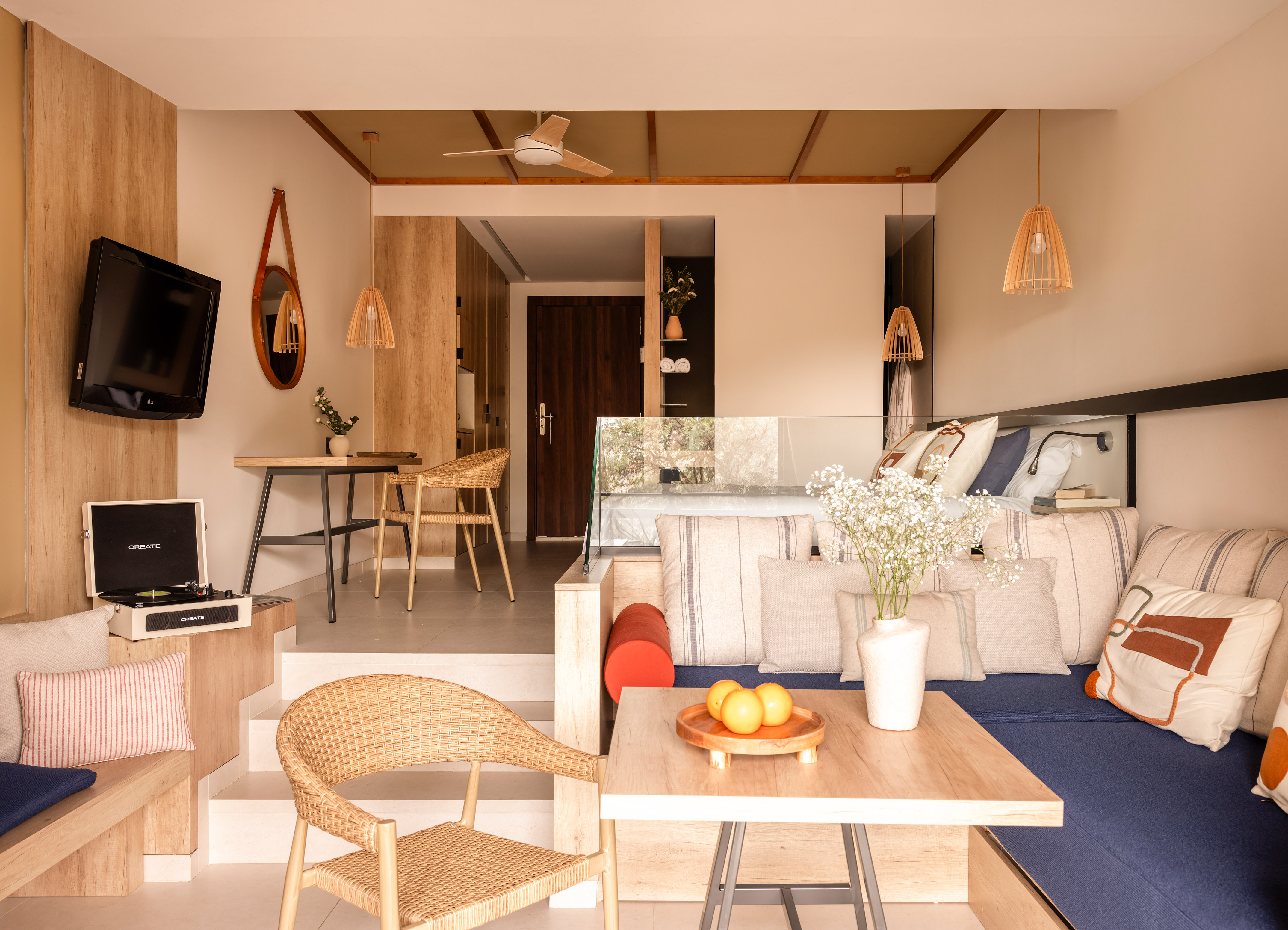Modern hotel suite with living, dining, and bed zones. Record player, wood, wicker decor.