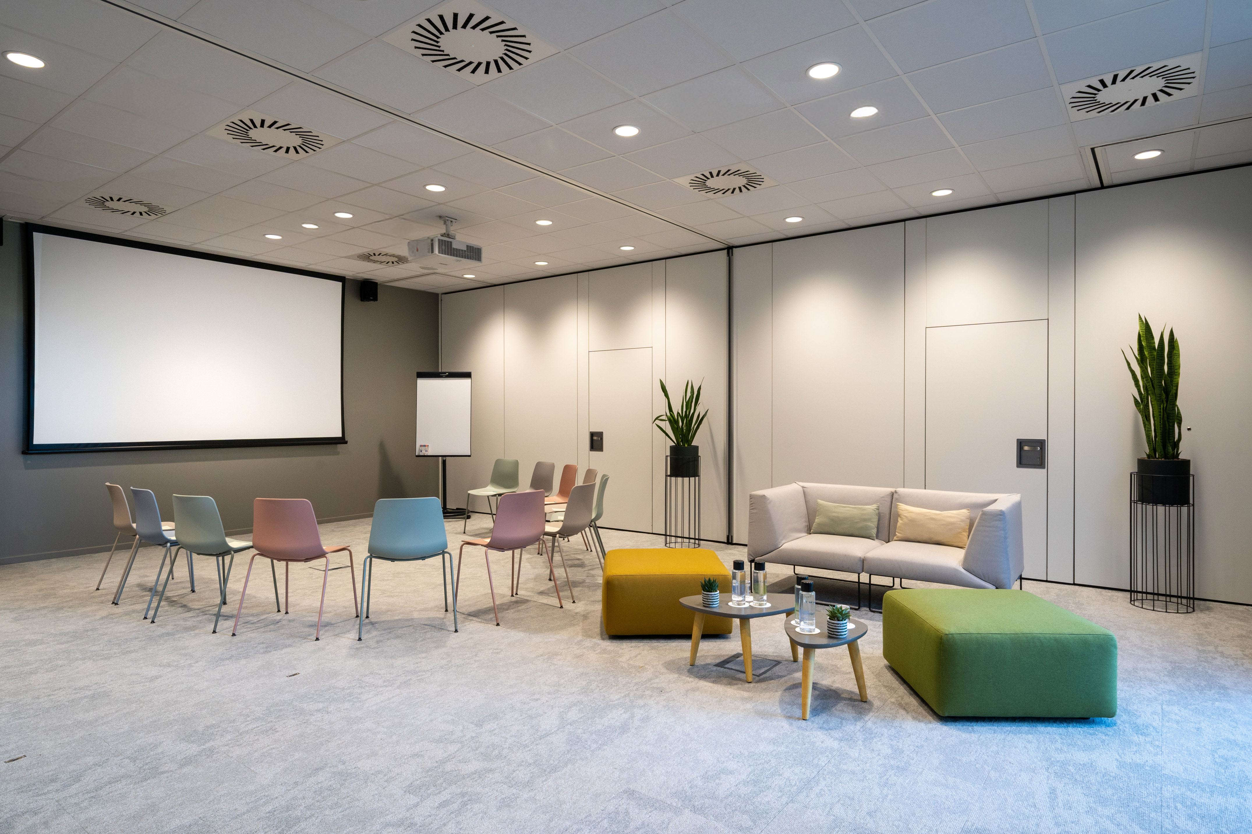 Flexible meeting room with projector screen, colorful chairs, and lounge area.