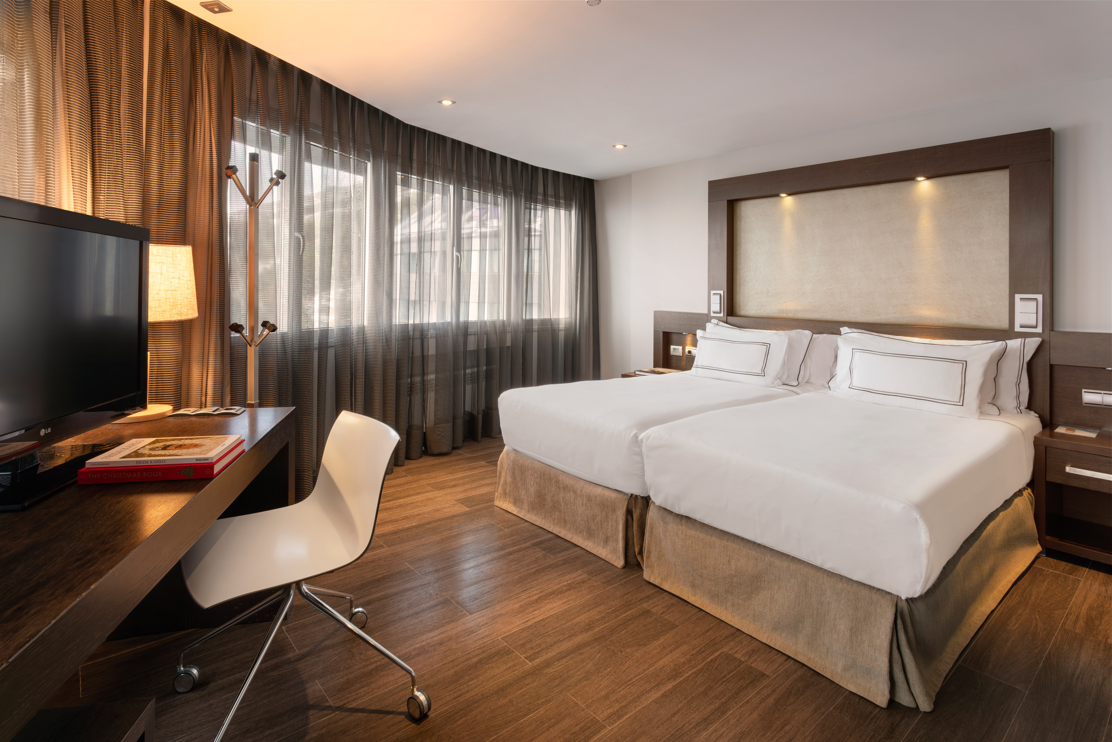Contemporary hotel guest room with two beds, workspace, TV, and large windows.