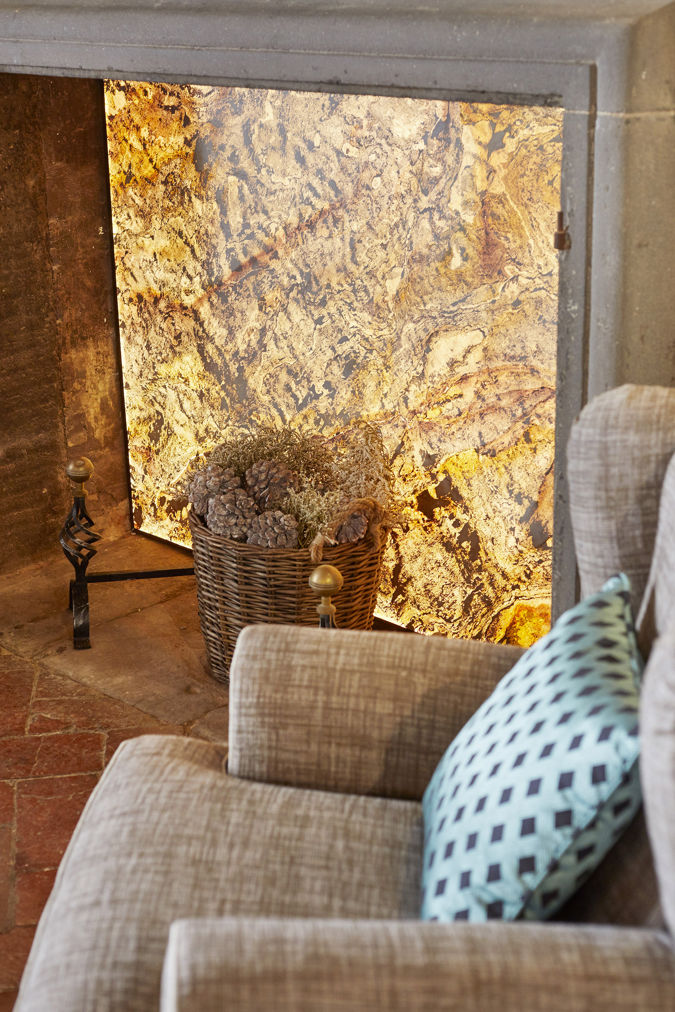 Fireplace with glowing textured backdrop, pinecones in basket, and cozy sofa.
