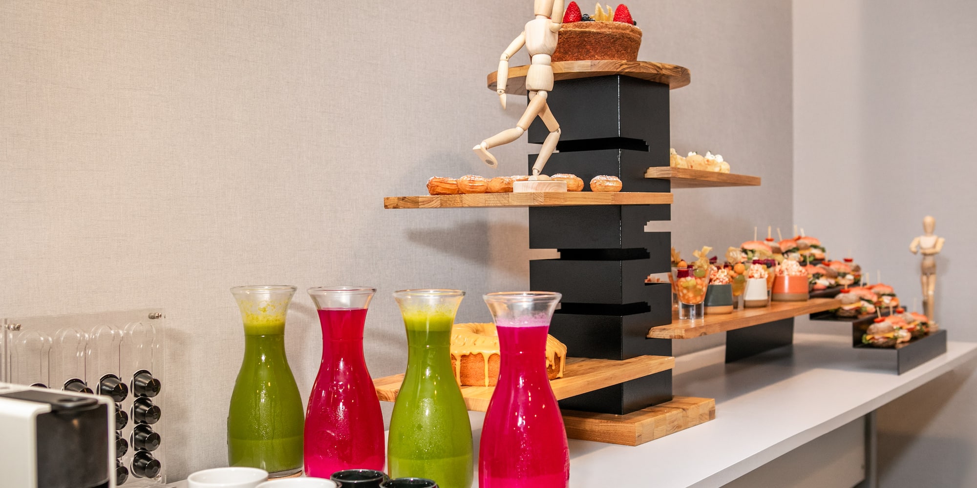Fresh juices, pastries, and sandwiches on a modern tiered catering buffet.
