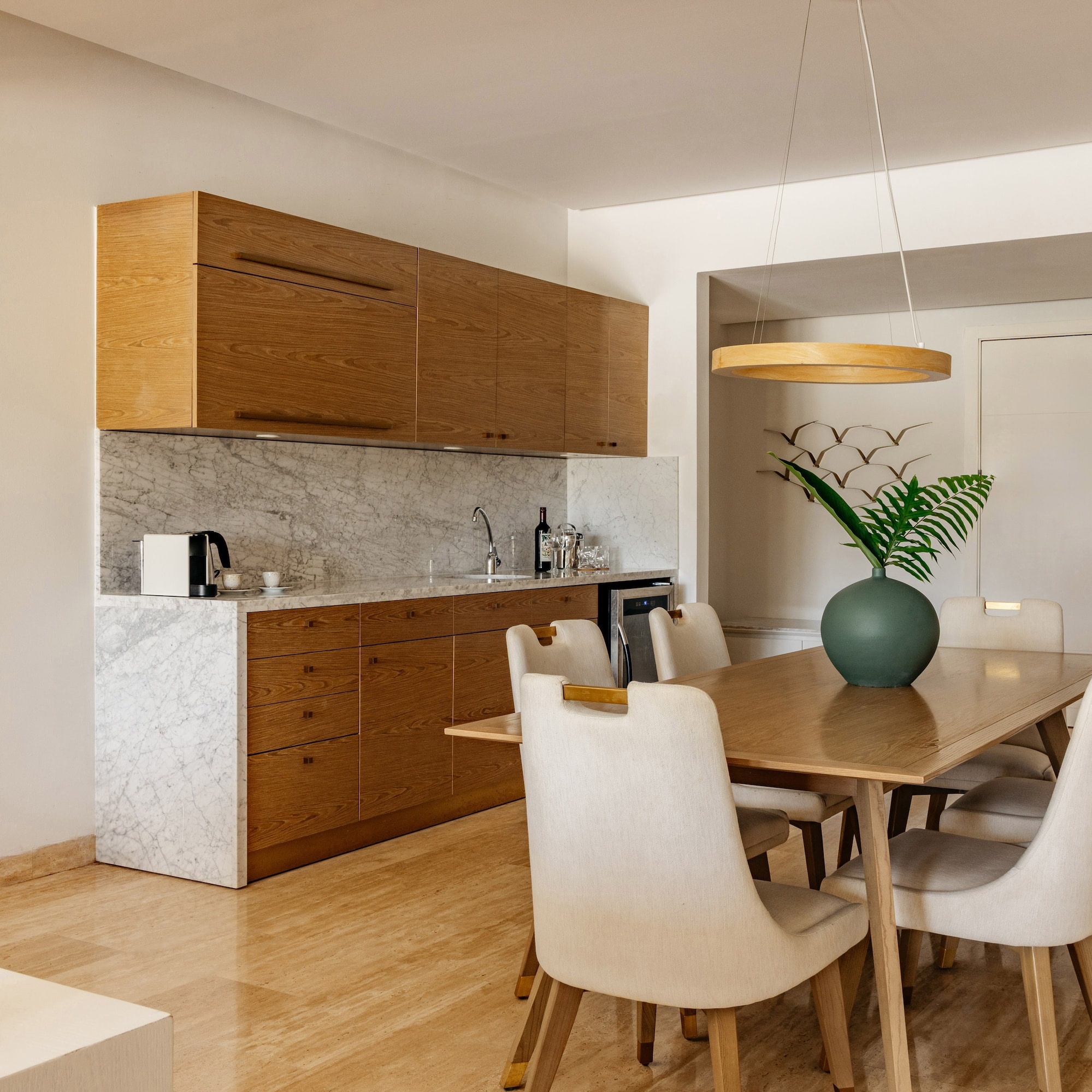 Modern kitchen dining area featuring wood cabinets, marble, and upholstered chairs.