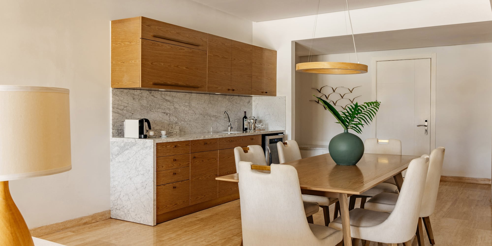 Modern kitchenette and dining area with wooden cabinets and marble counter.