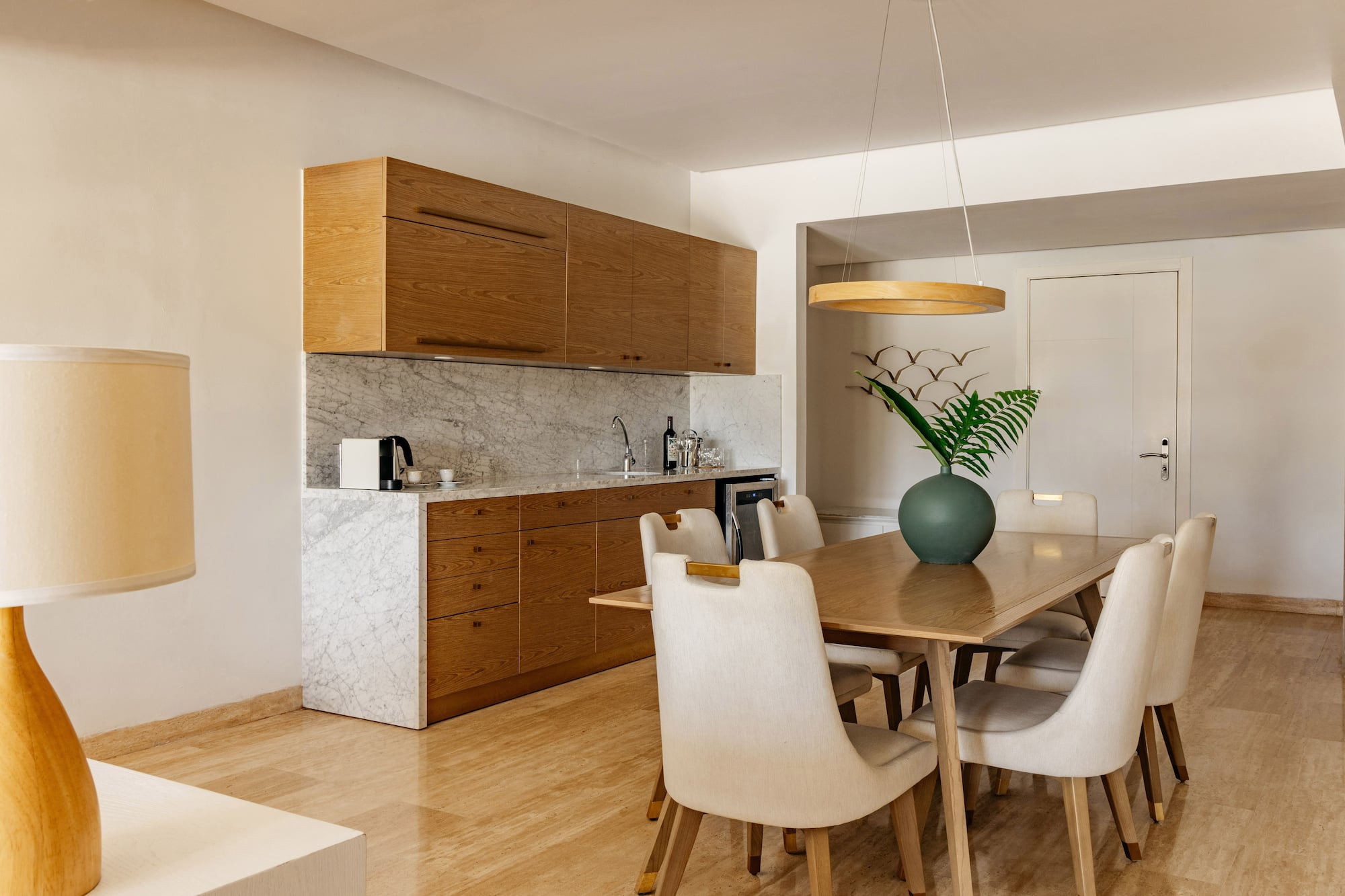 Modern kitchenette and dining area with wooden cabinets and marble counter.