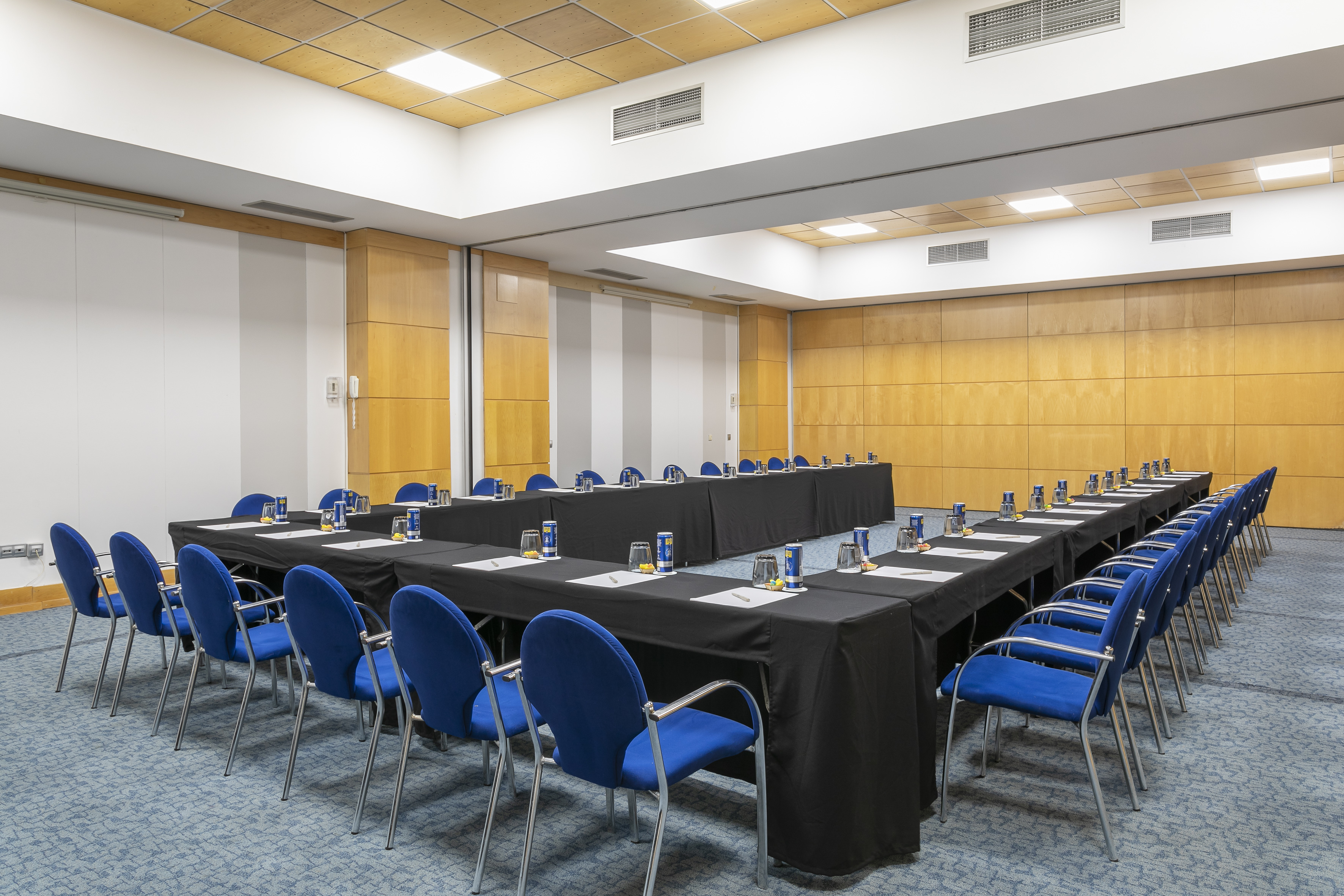 U-shaped conference room with blue chairs, black tables, and wood paneled walls.
