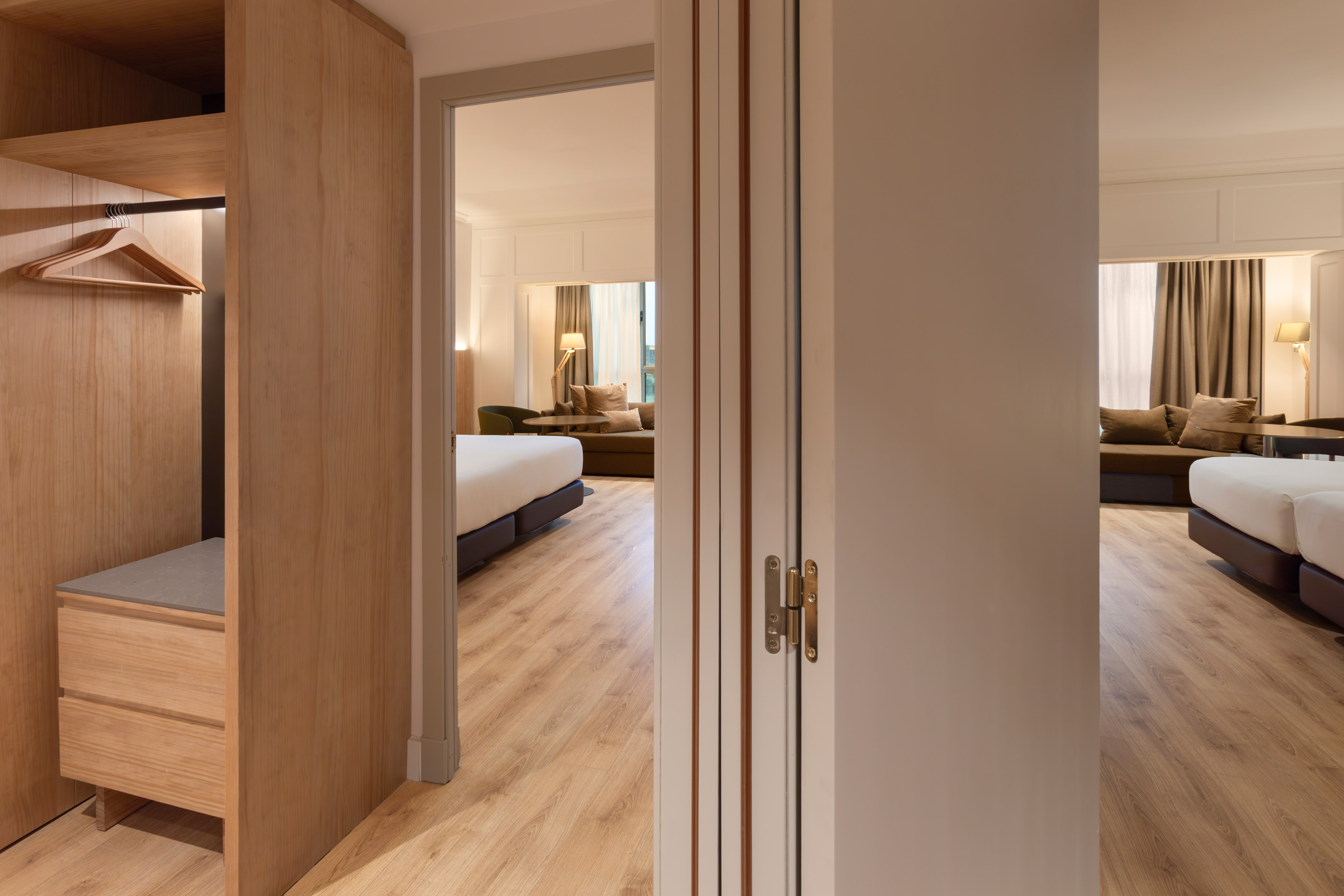 Modern hotel suite with open wardrobe, bed, and sofa area.