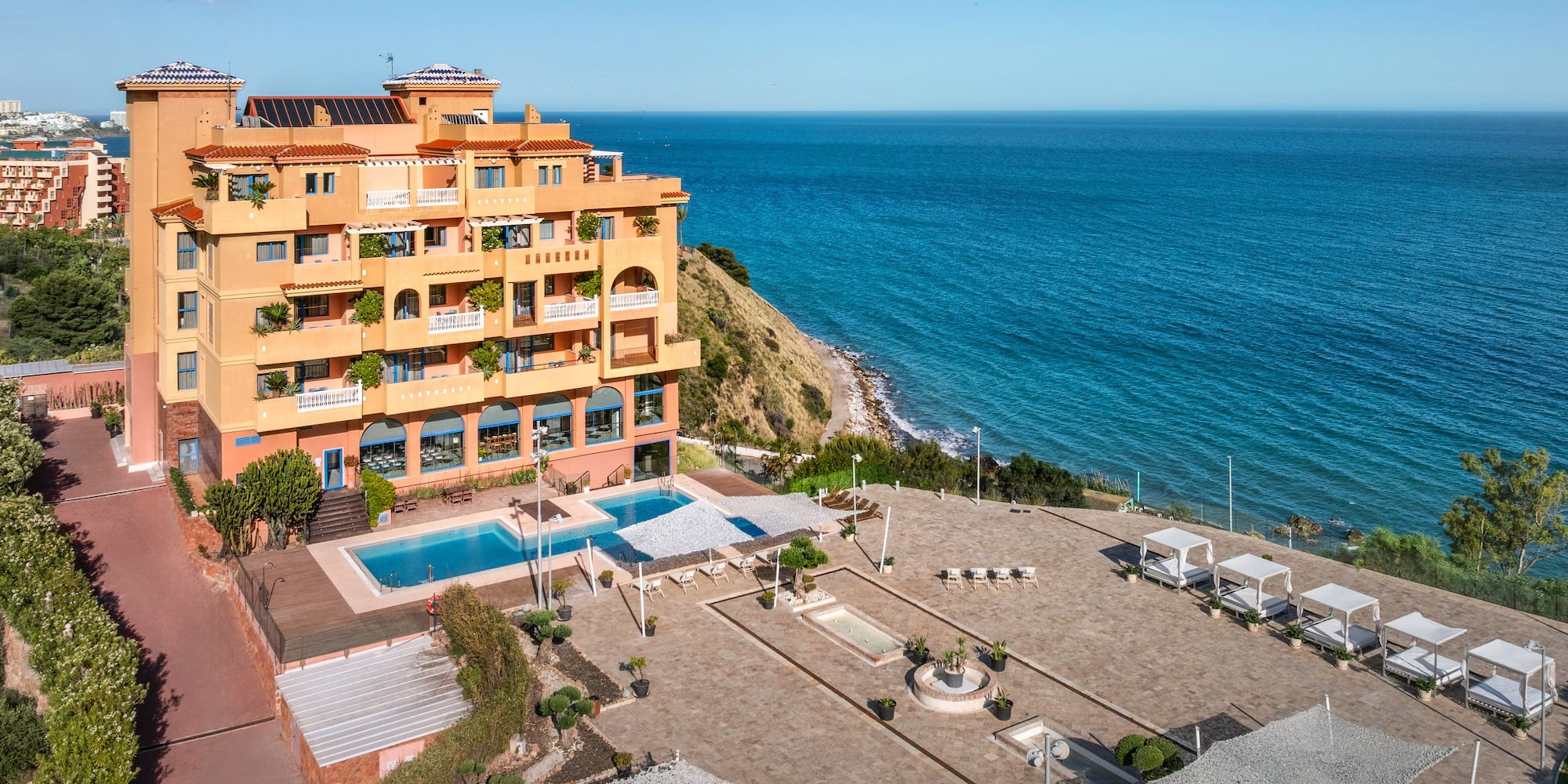Oceanfront hotel with pool, sunbeds, and clear blue sea.