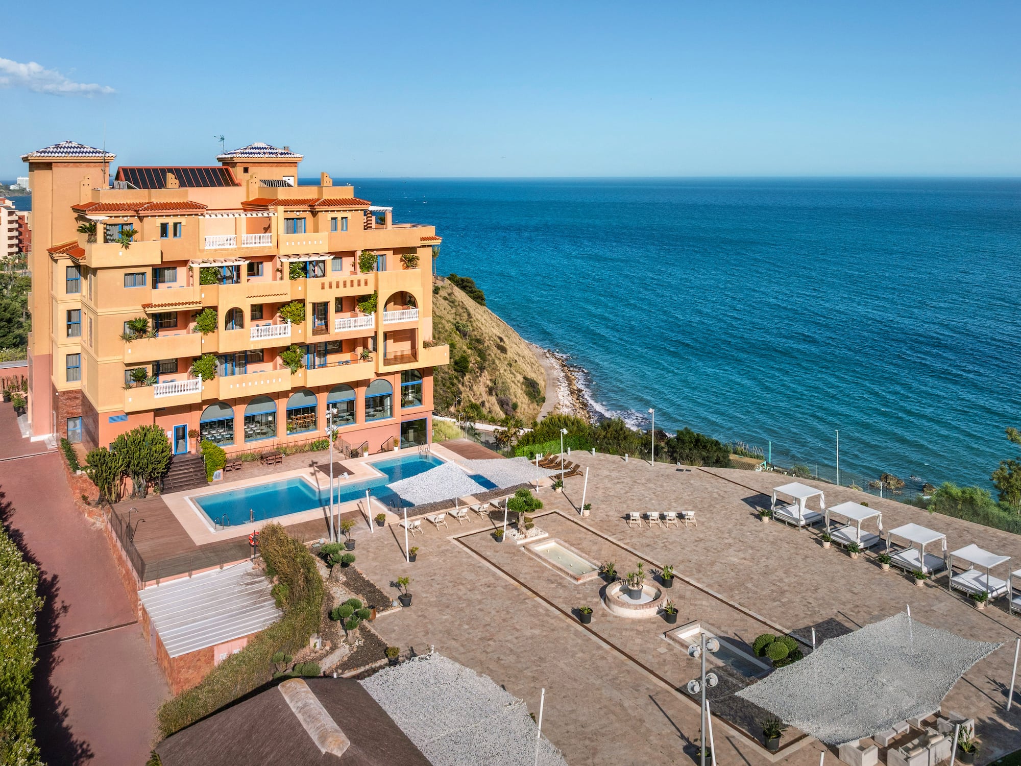 Oceanfront hotel with pool, sunbeds, and clear blue sea.