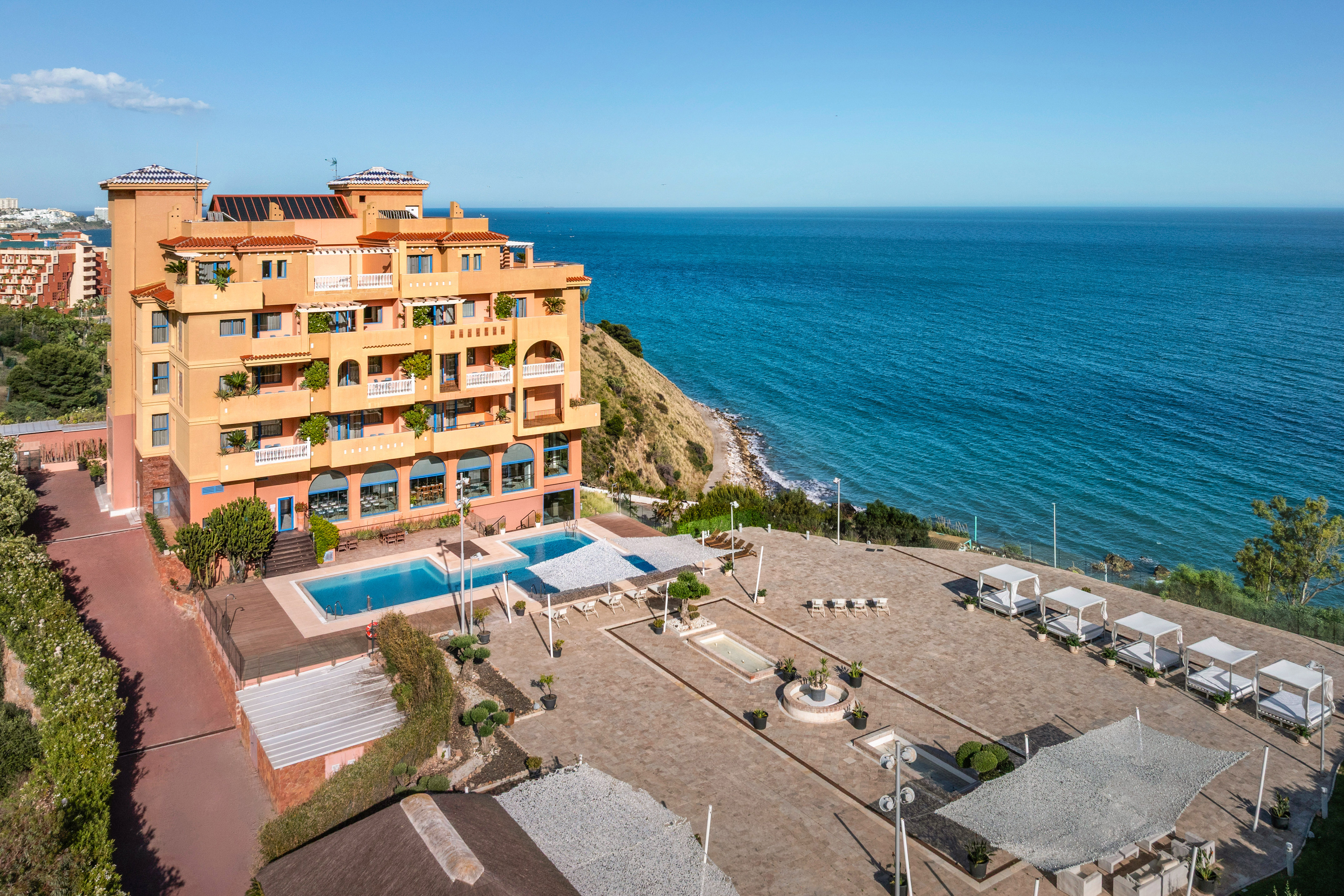 Oceanfront hotel with pool, sunbeds, and clear blue sea.