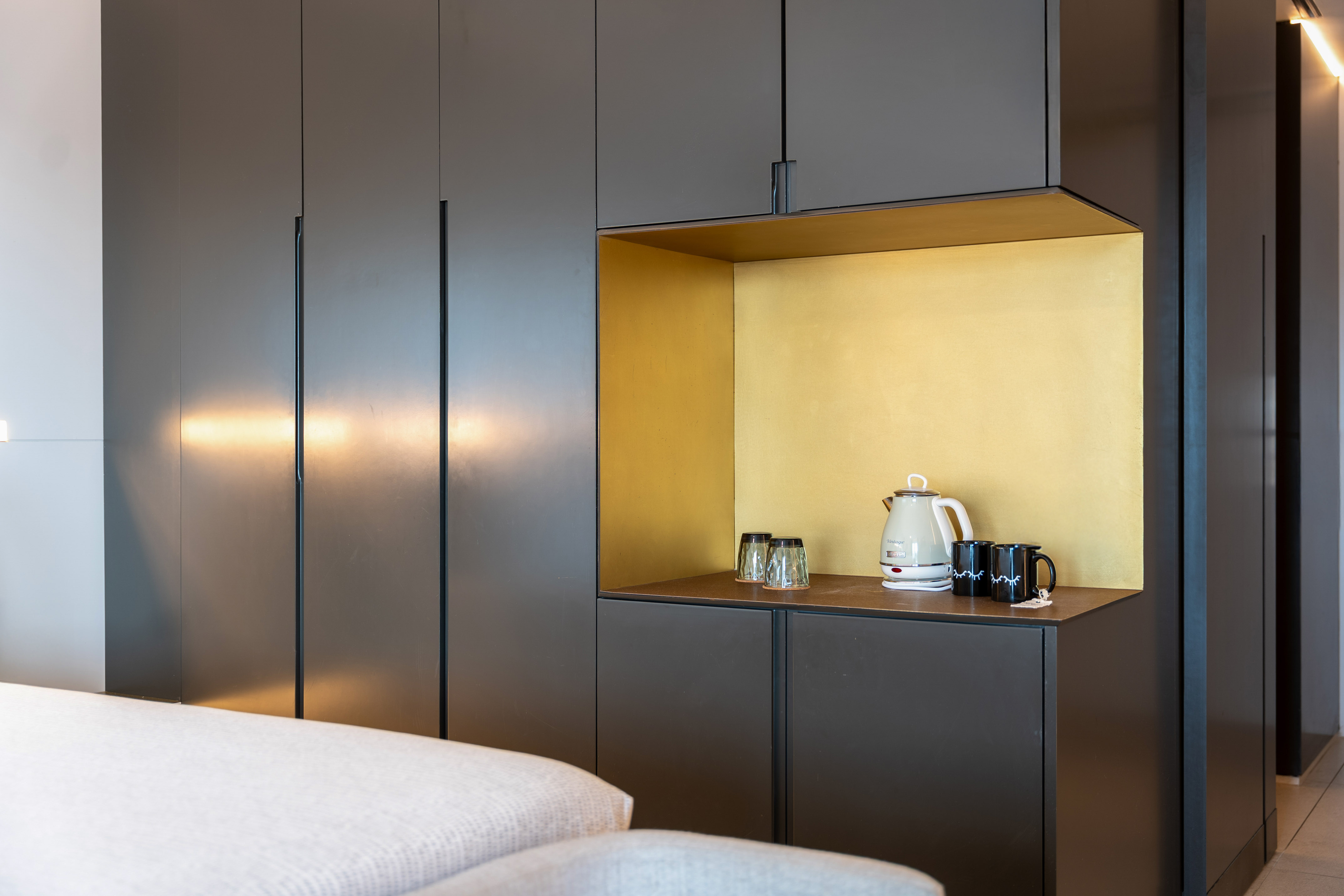 Dark grey modern cabinet, golden illuminated niche with kettle and mugs.