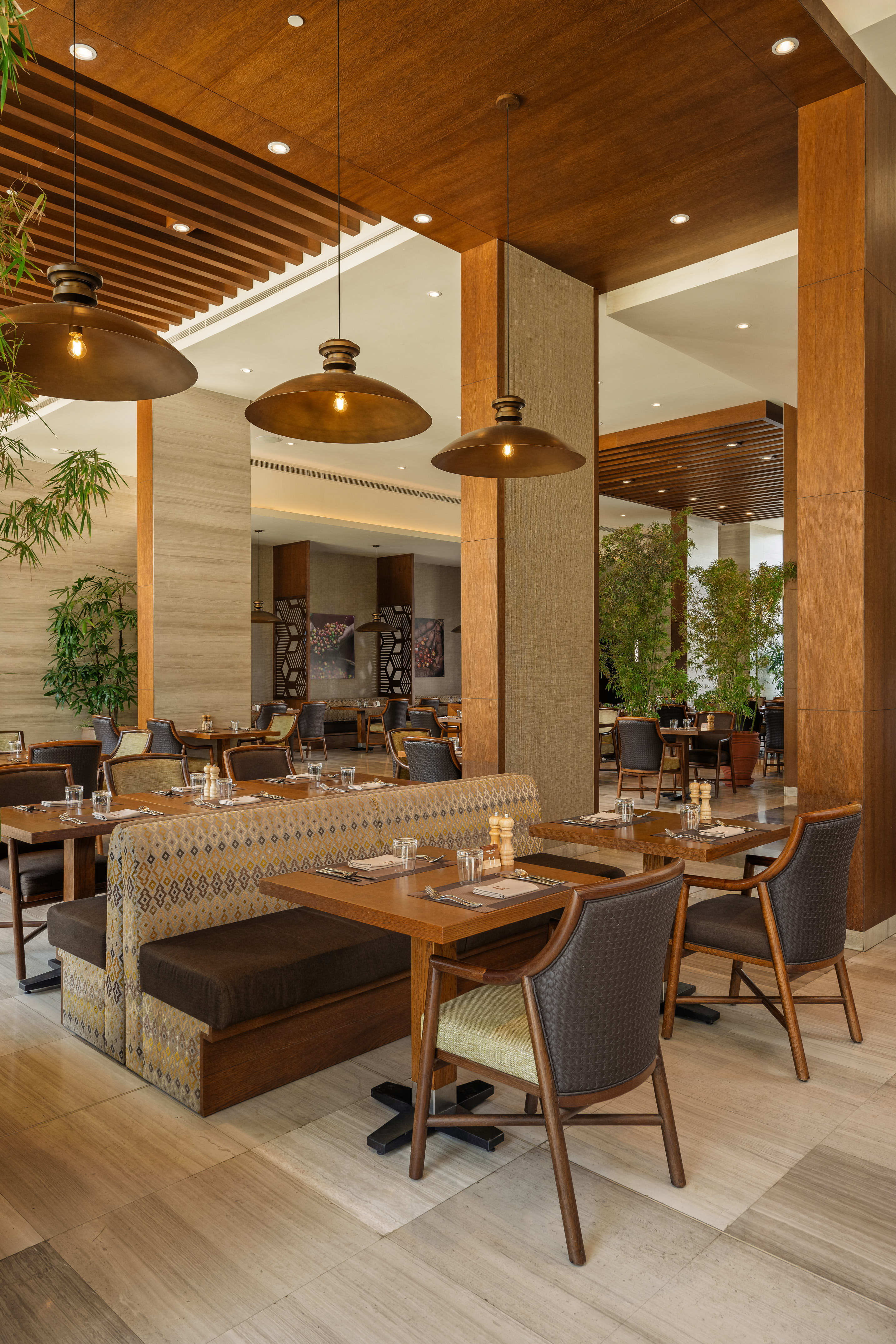 Modern restaurant dining room with wooden tables, booths, and pendant lights.