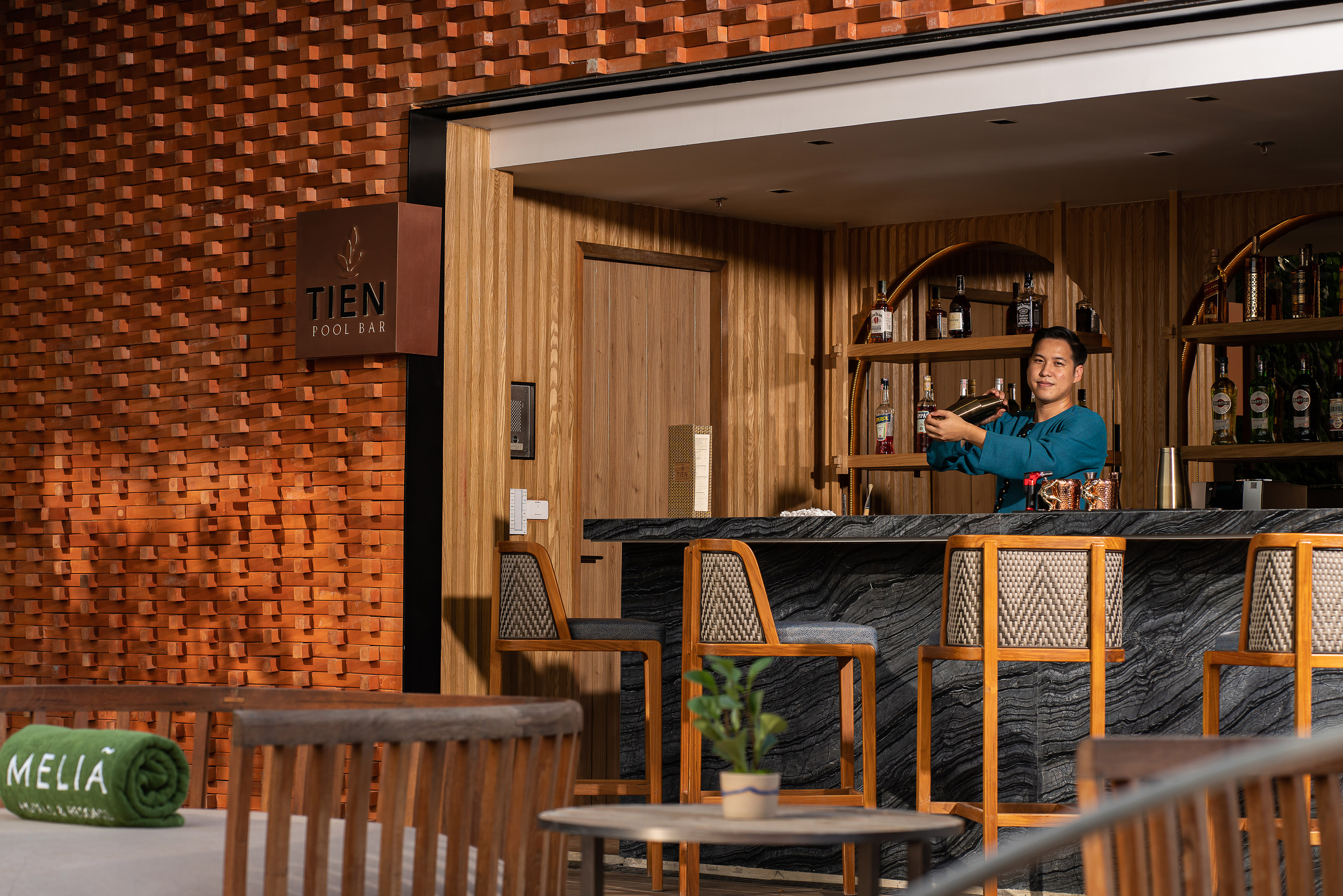 Bartender mixing cocktails at Meliá's Tien Pool Bar, distinctive brick wall.