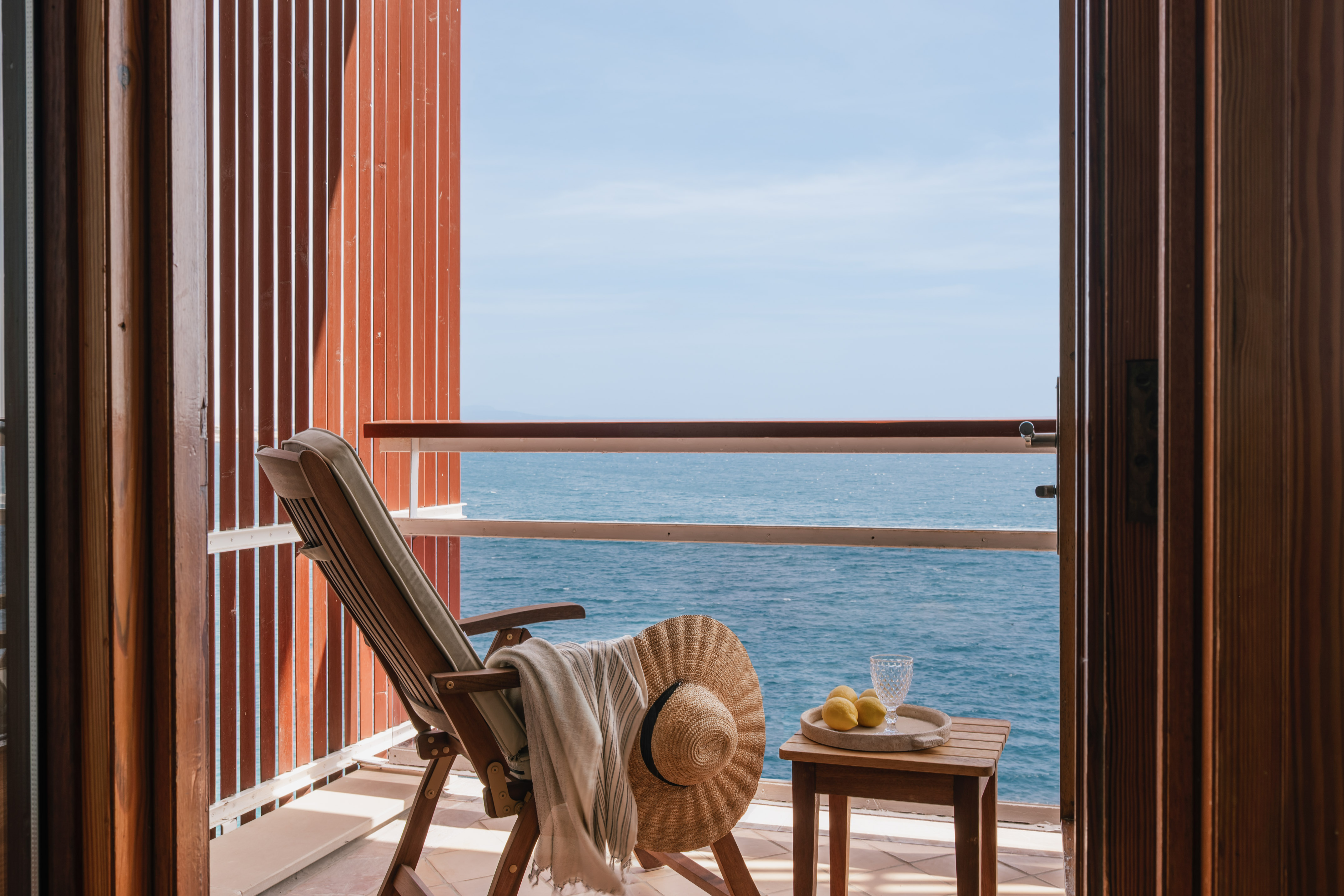 Coastal balcony with sea view, lounge chair, straw hat, and lemons.